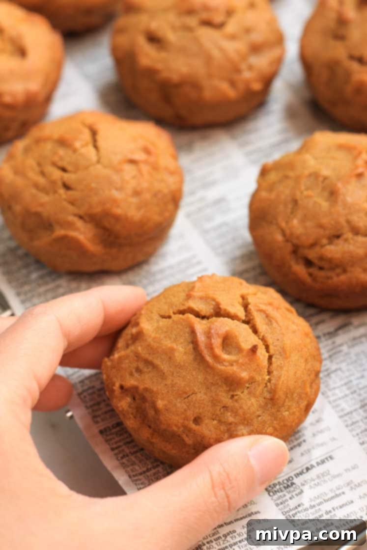 A hand gently reaching for a perfectly baked gluten-free pumpkin muffin on a wire cooling rack.
