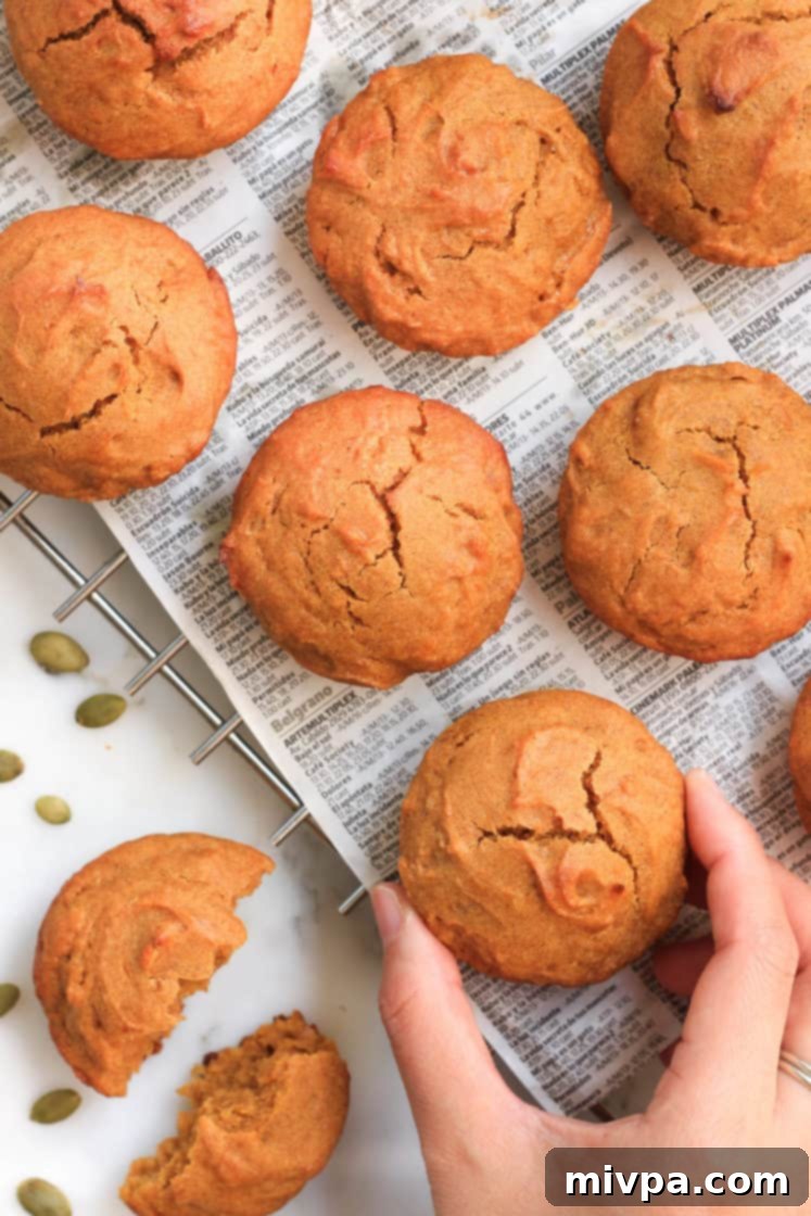 A hand reaching for a perfectly golden-brown vegan gluten-free pumpkin muffin on a wire cooling rack, ready to be enjoyed.