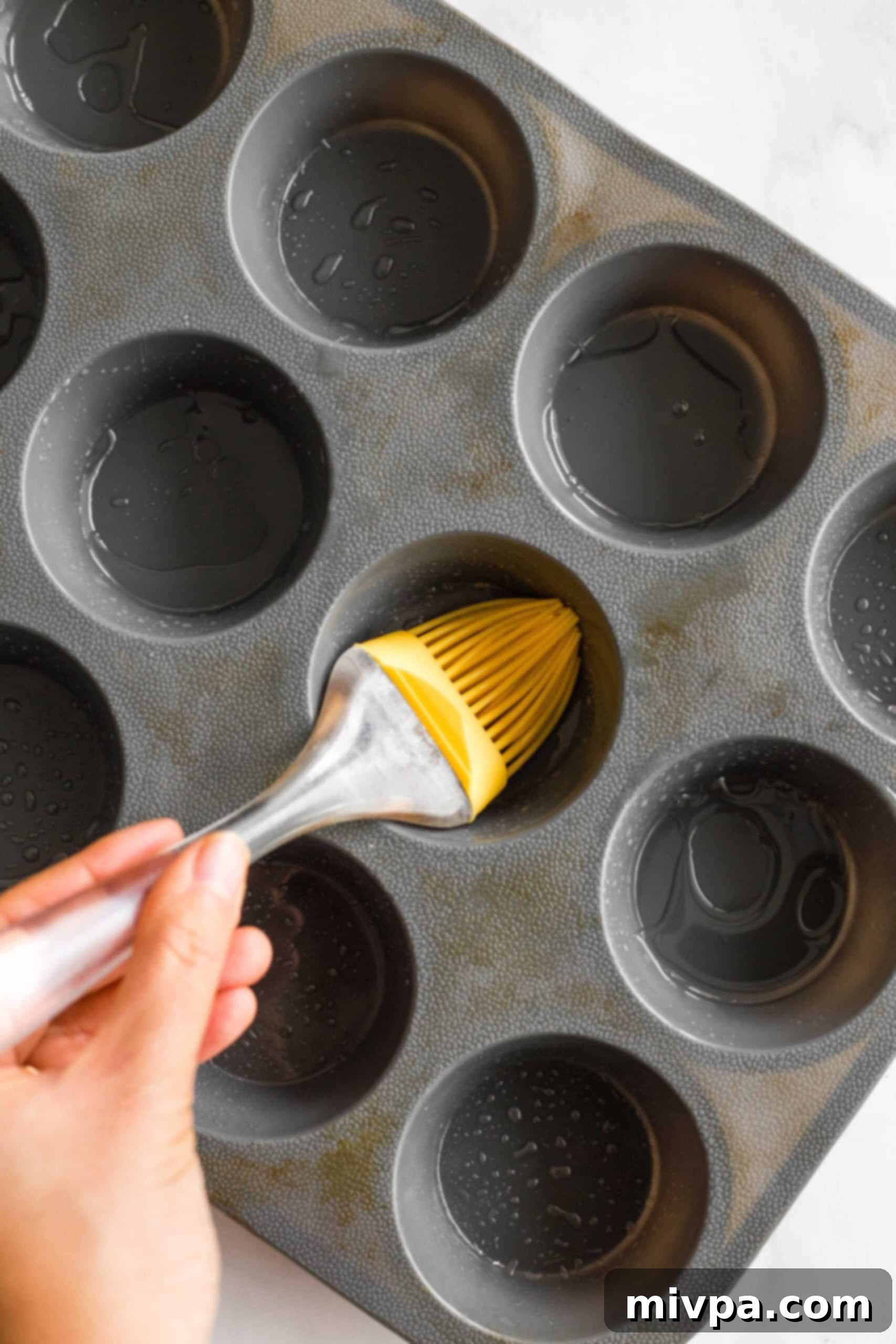 A silicon brush meticulously greasing a silicon muffin mold, preparing it for the pumpkin muffin batter.