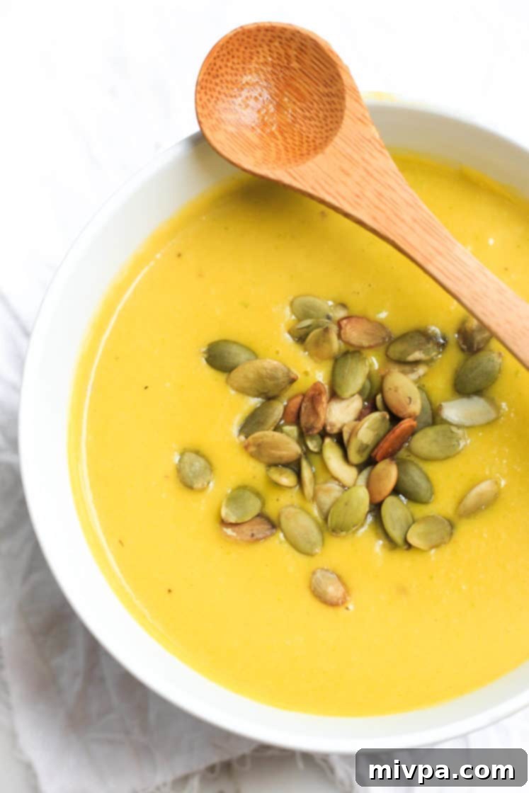 Gluten-Free Pumpkin Soup (Dairy-free, Vegan) Pumpkin soup with pumpkin seeds in a bowl with a wooden spoon.