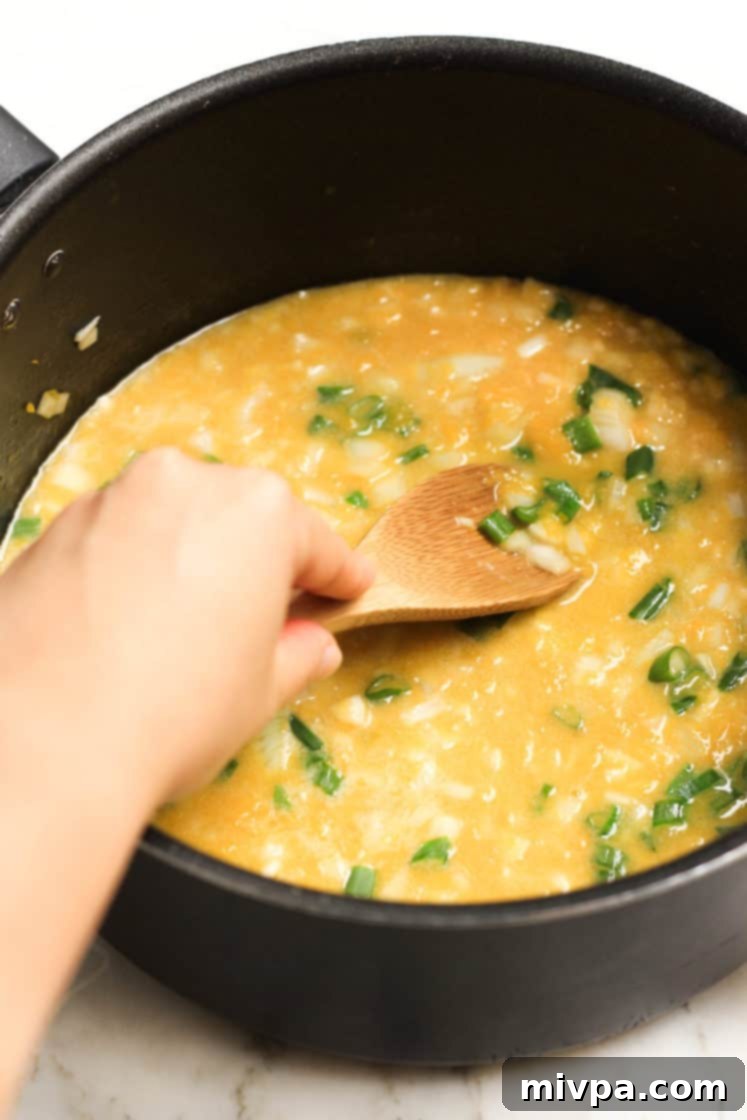 Gluten-Free Vegan Pumpkin Soup (Dairy-Free) Hand mixing the ingredients in a pot of dairy-free pumpkin soup.