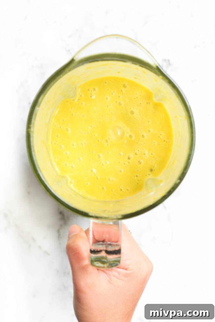 Creamy Vegan Pumpkin Soup (Gluten-free) Hand holding a blender with just-blended pumpkin soup.