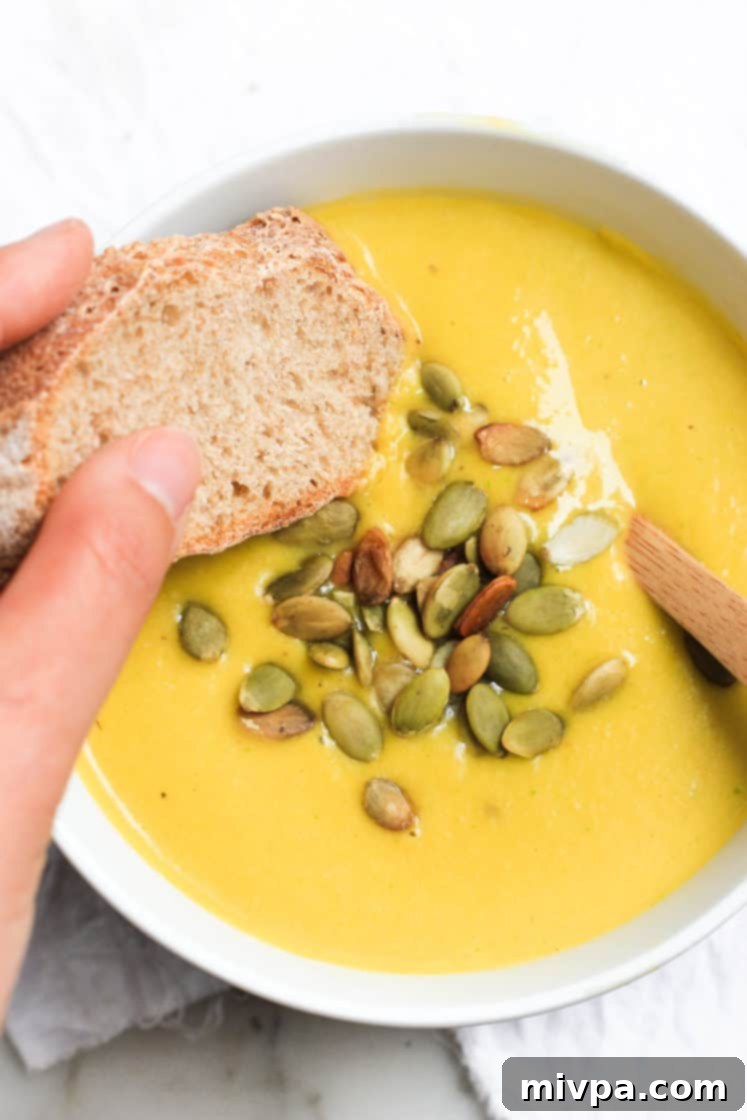Creamy Pumpkin Soup (Gluten-free, Vegan) Hand dipping a slice of bread into a bowl of soup.