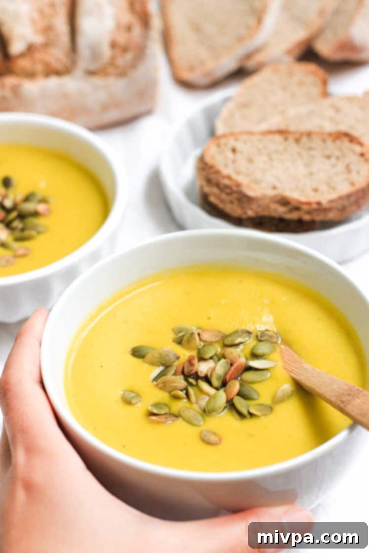 Creamy Pumpkin Soup (Gluten-free, Vegan) Hand holding a bowl of creamy soup.