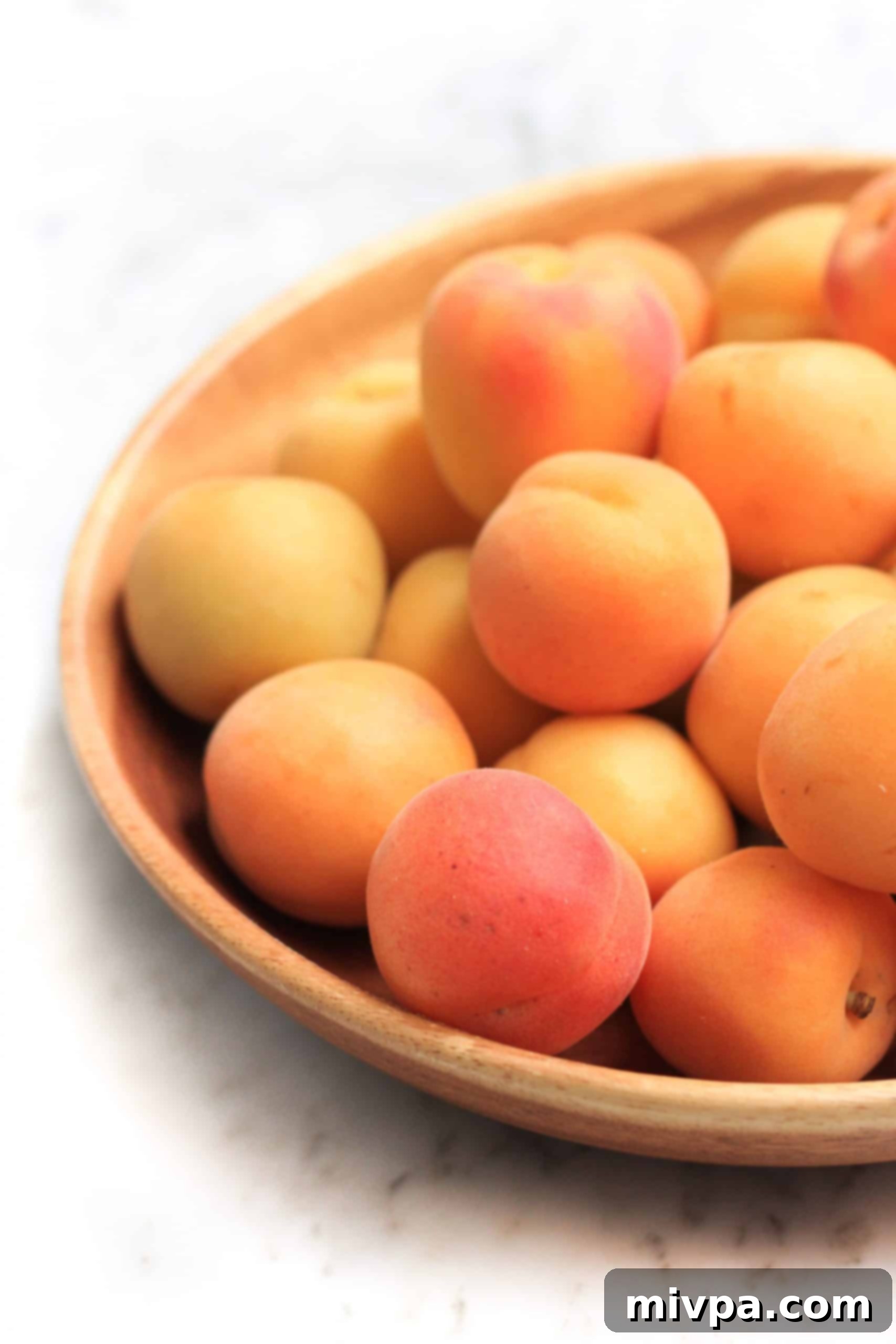 A large wooden bowl full of fresh apricots.