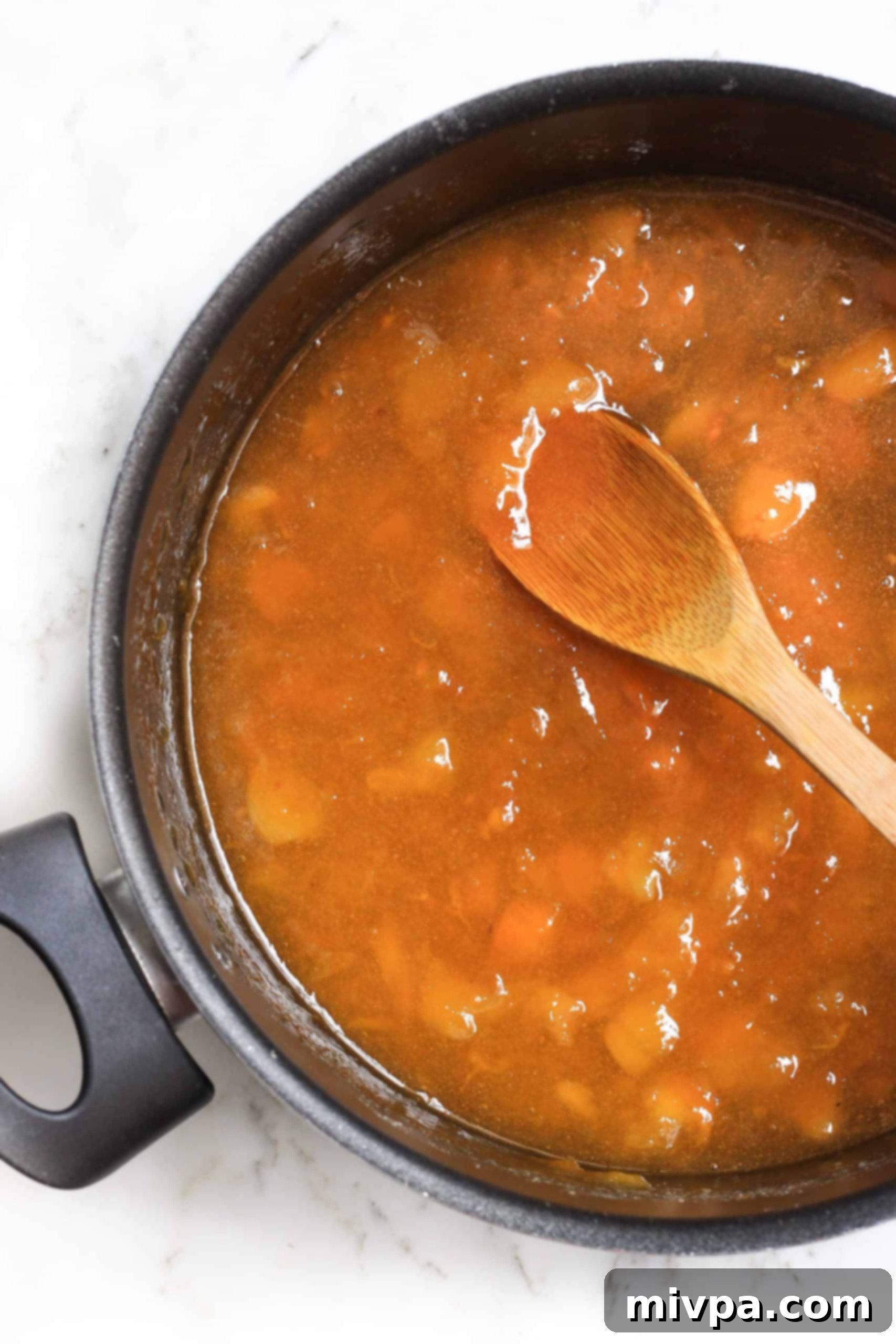 A wooden spoon in a large pot of homemade apricot preserves.