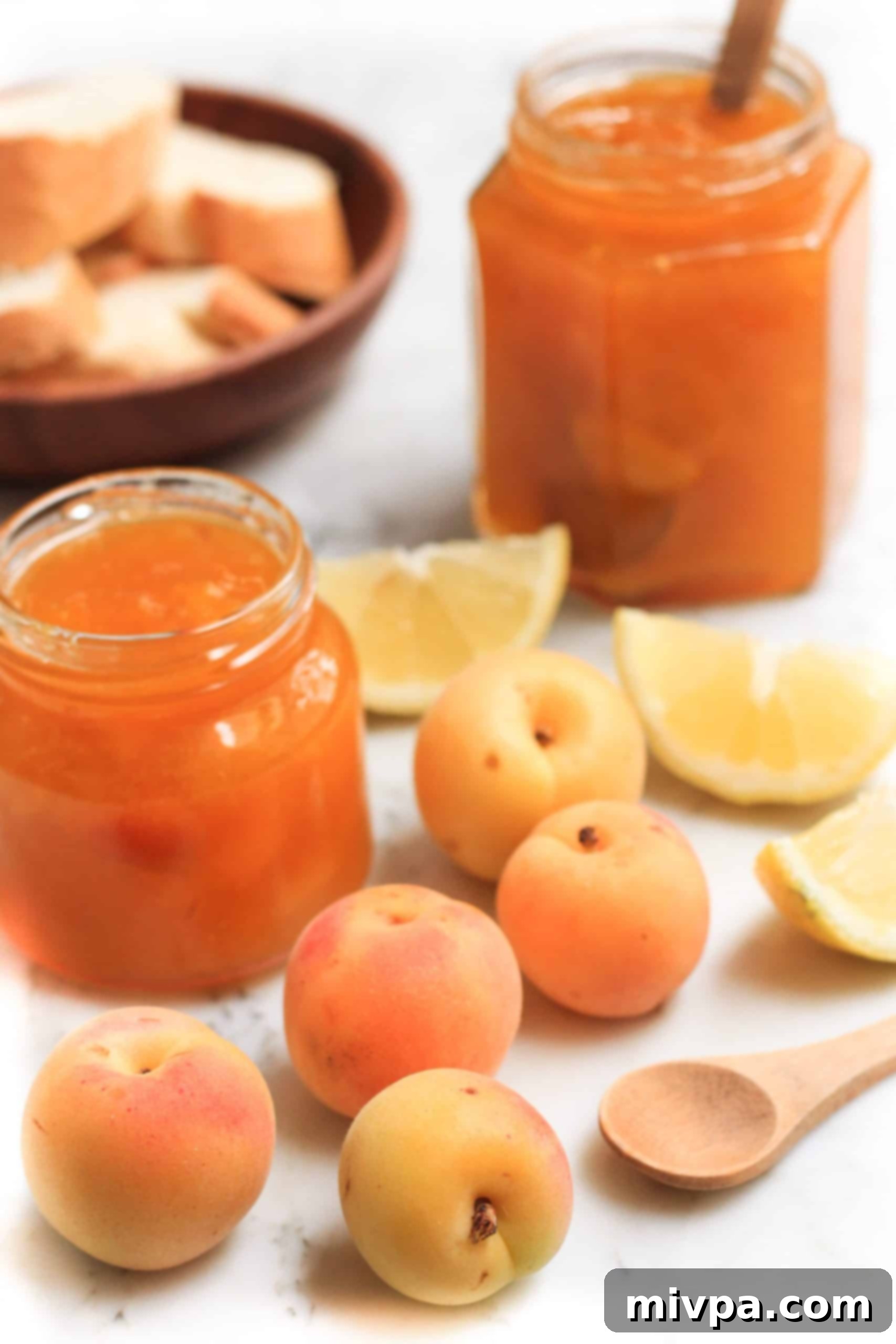 A jar of jam, fresh apricots and lemons on a marble board.