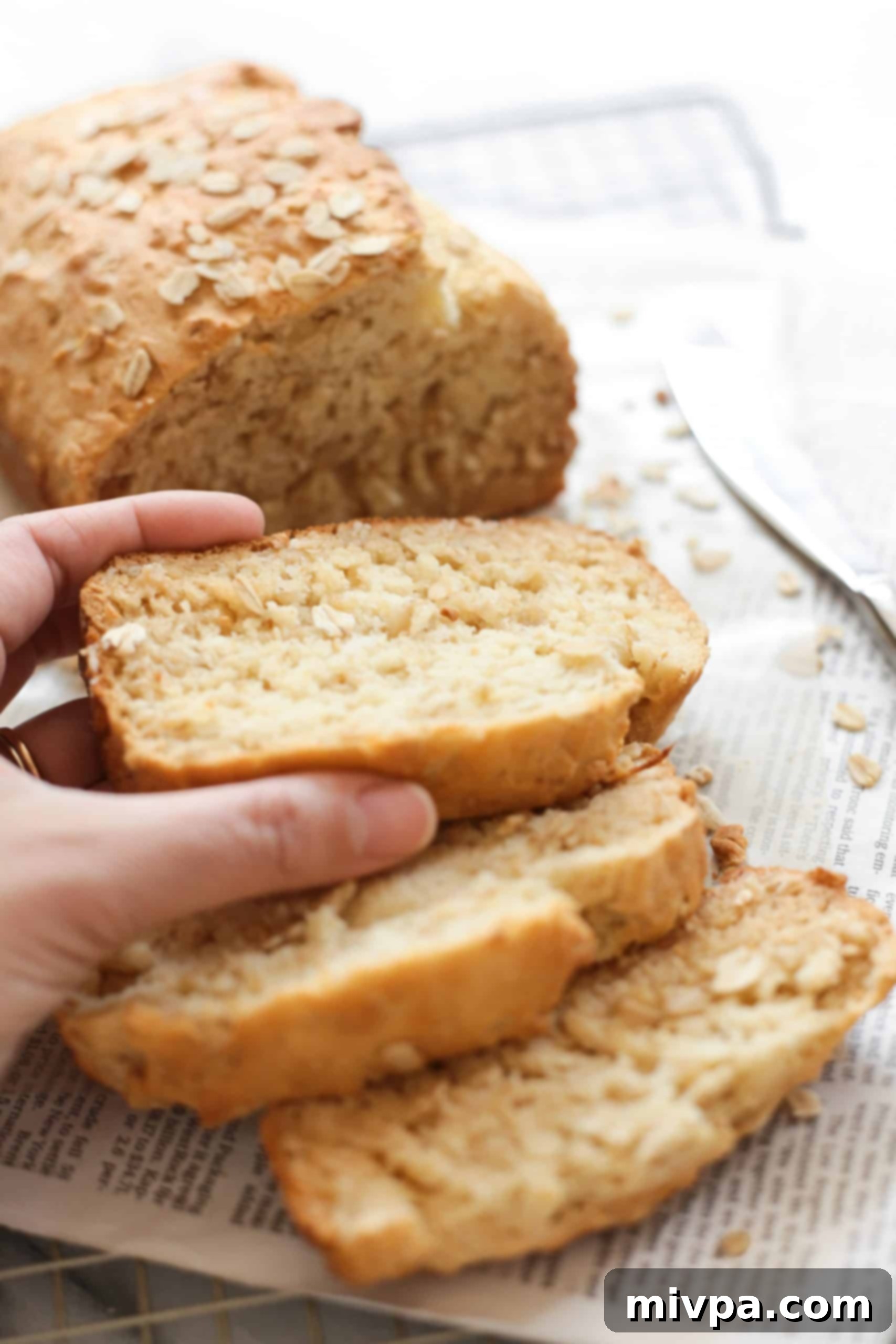 Hand holding a slice of gluten-free oat bread, showcasing its moist and fluffy texture.