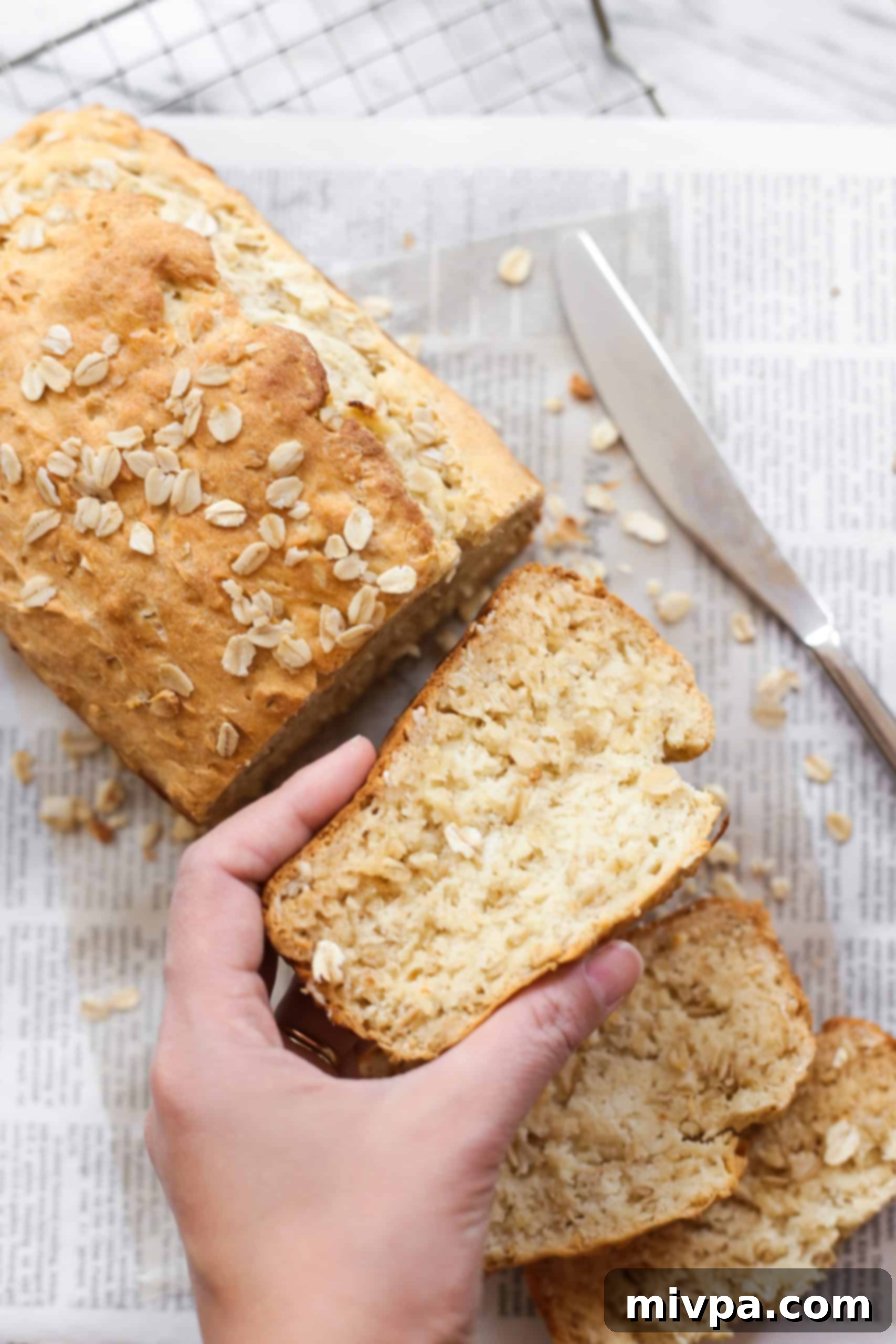 Hand holding up a perfectly sliced piece of honey oat bread, showing its tender interior.
