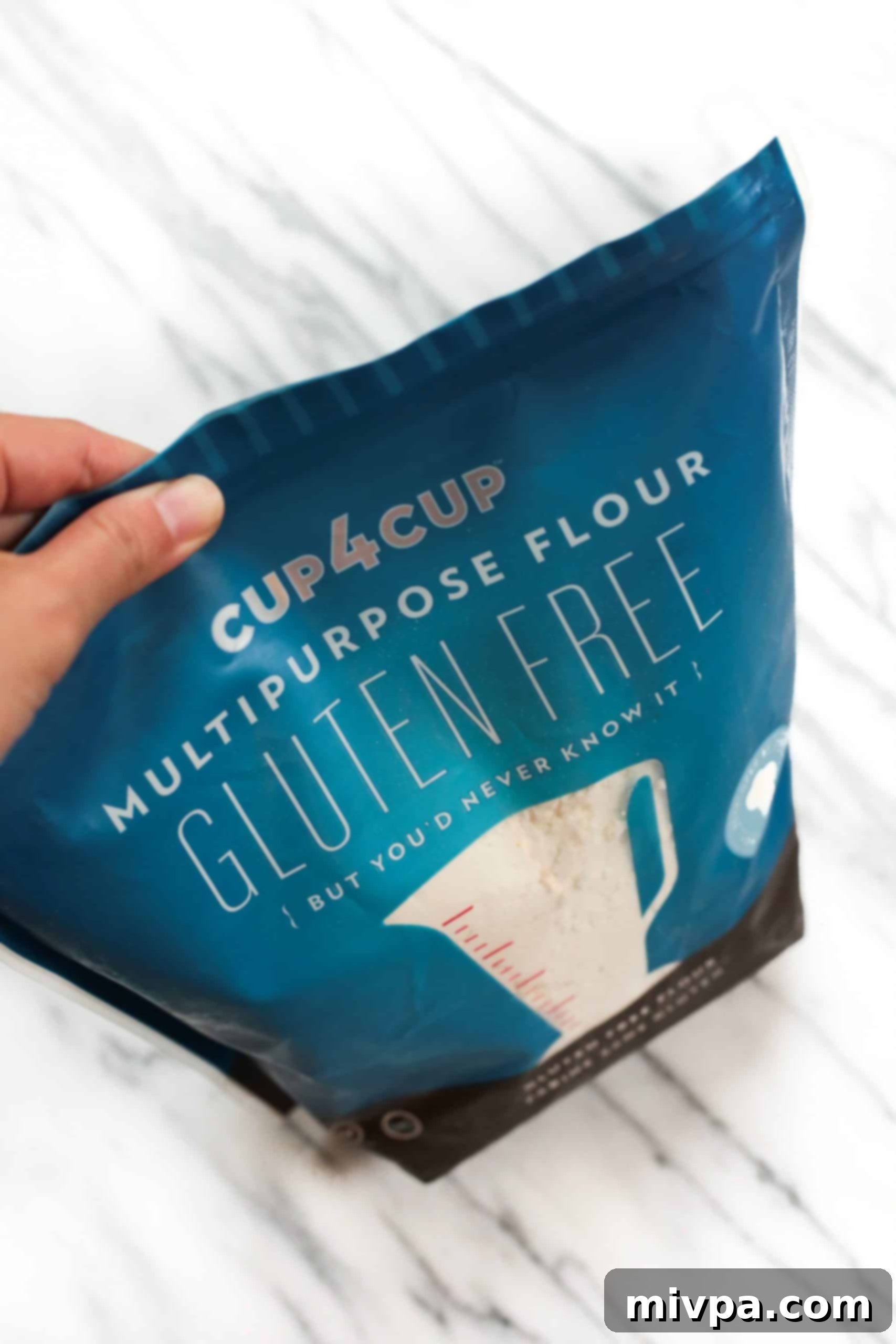 A hand holding a bag of Cup4Cup gluten-free flour, highlighting the key ingredient.