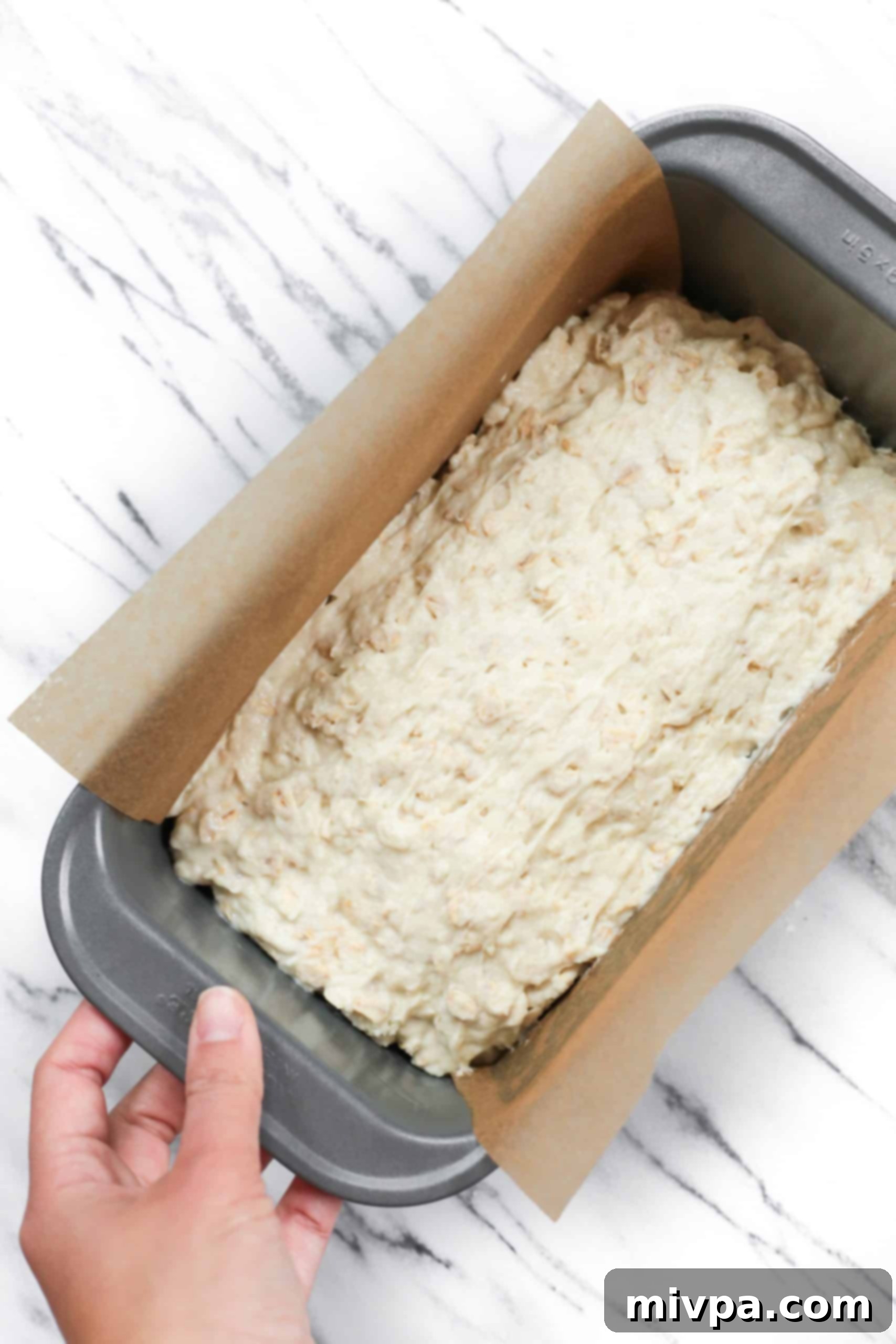 Oat bread batter poured into a parchment-lined loaf pan, ready for baking.