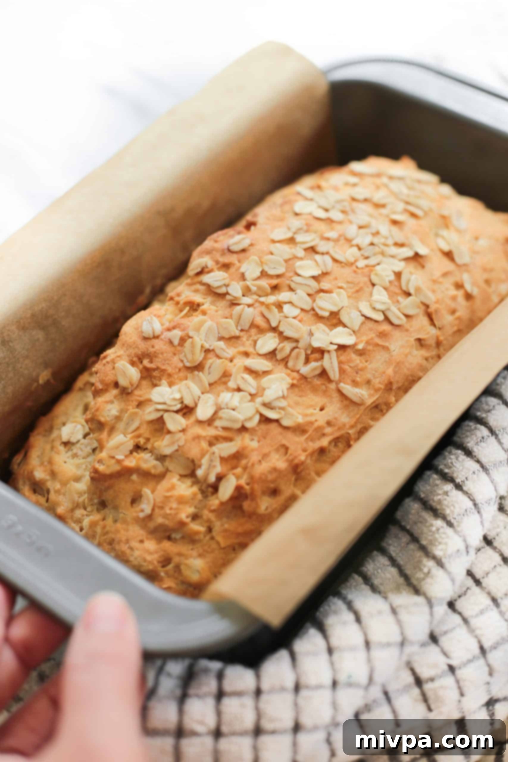 A freshly baked, golden brown honey oatmeal bread loaf still in its pan, just out of the oven.