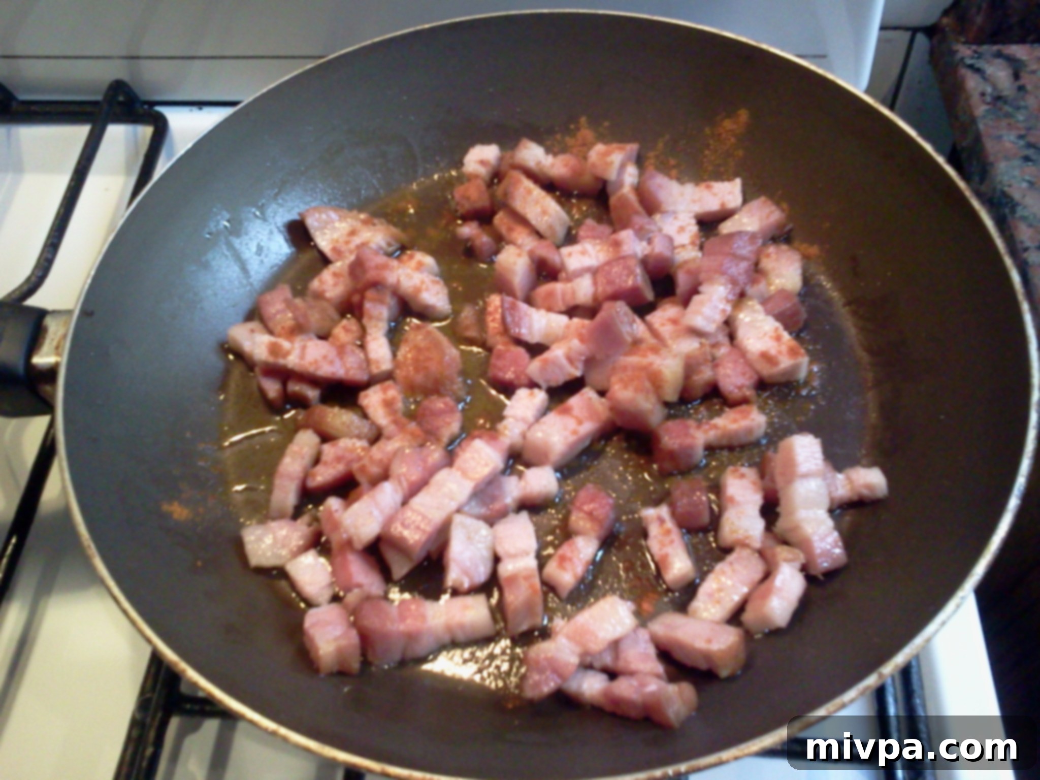 Cooked bacon in a pan with freshly added ground red pepper, being stirred.