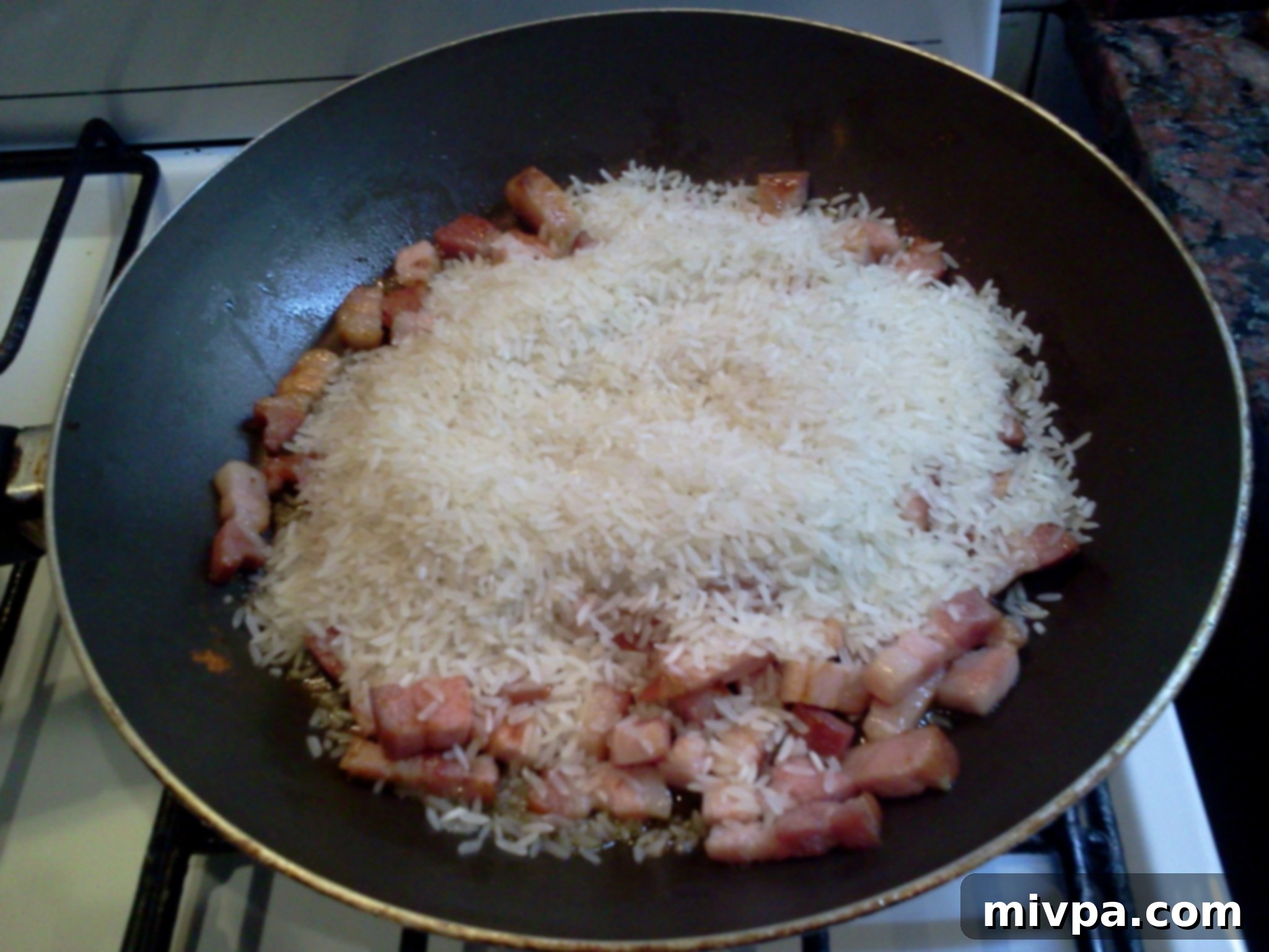 Raw long grain white rice added to the pan with cooked bacon and red pepper.