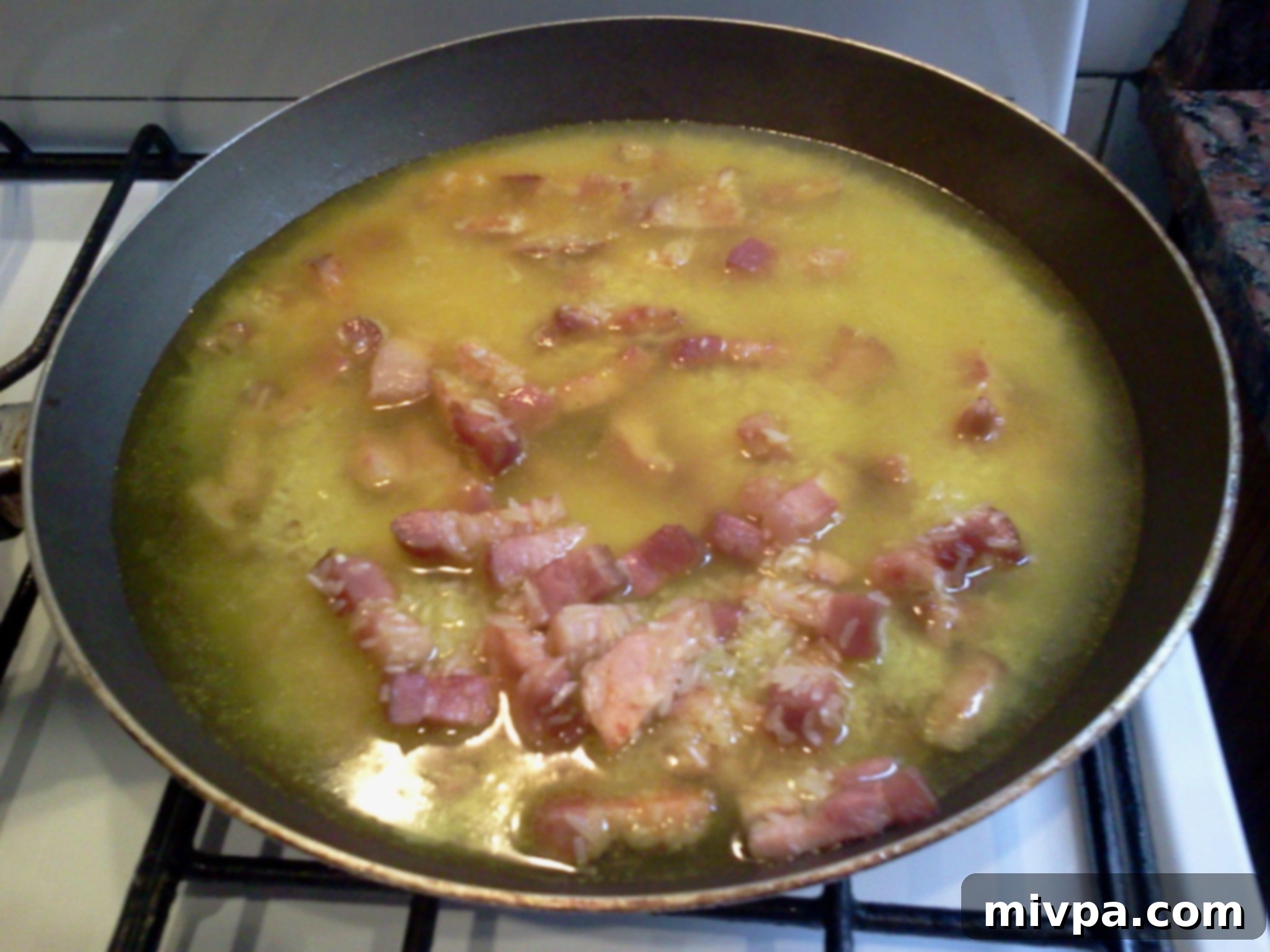 Saffron and water being poured into the pan with rice and bacon, beginning the infusion.