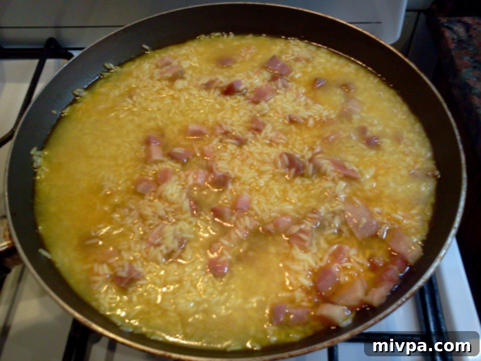 Rice grains visibly expanding and cooking in the pan, absorbing liquid and turning golden.