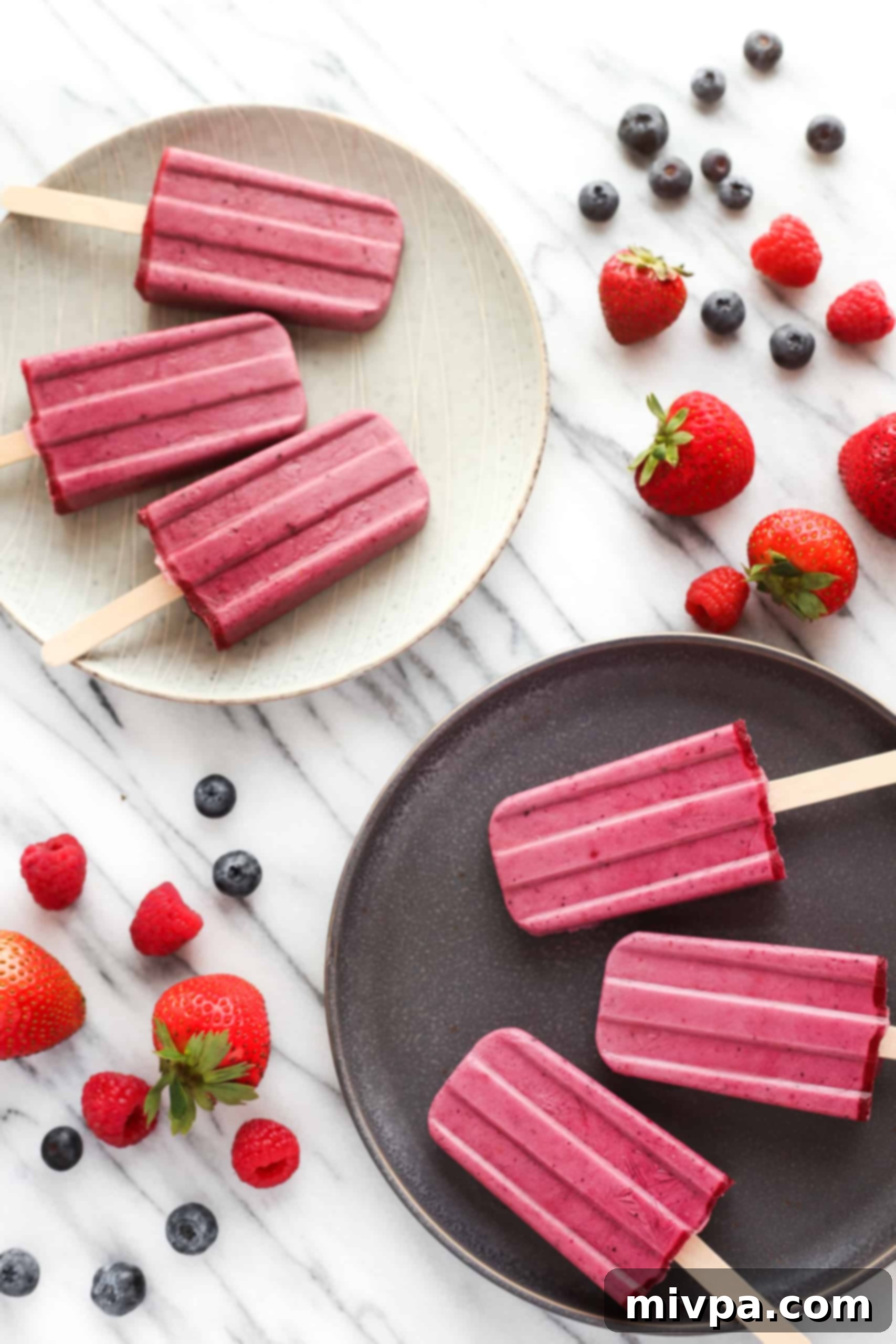 Plates of mixed berry yogurt popsicles on a marble board, showcasing their vibrant color and creamy texture.