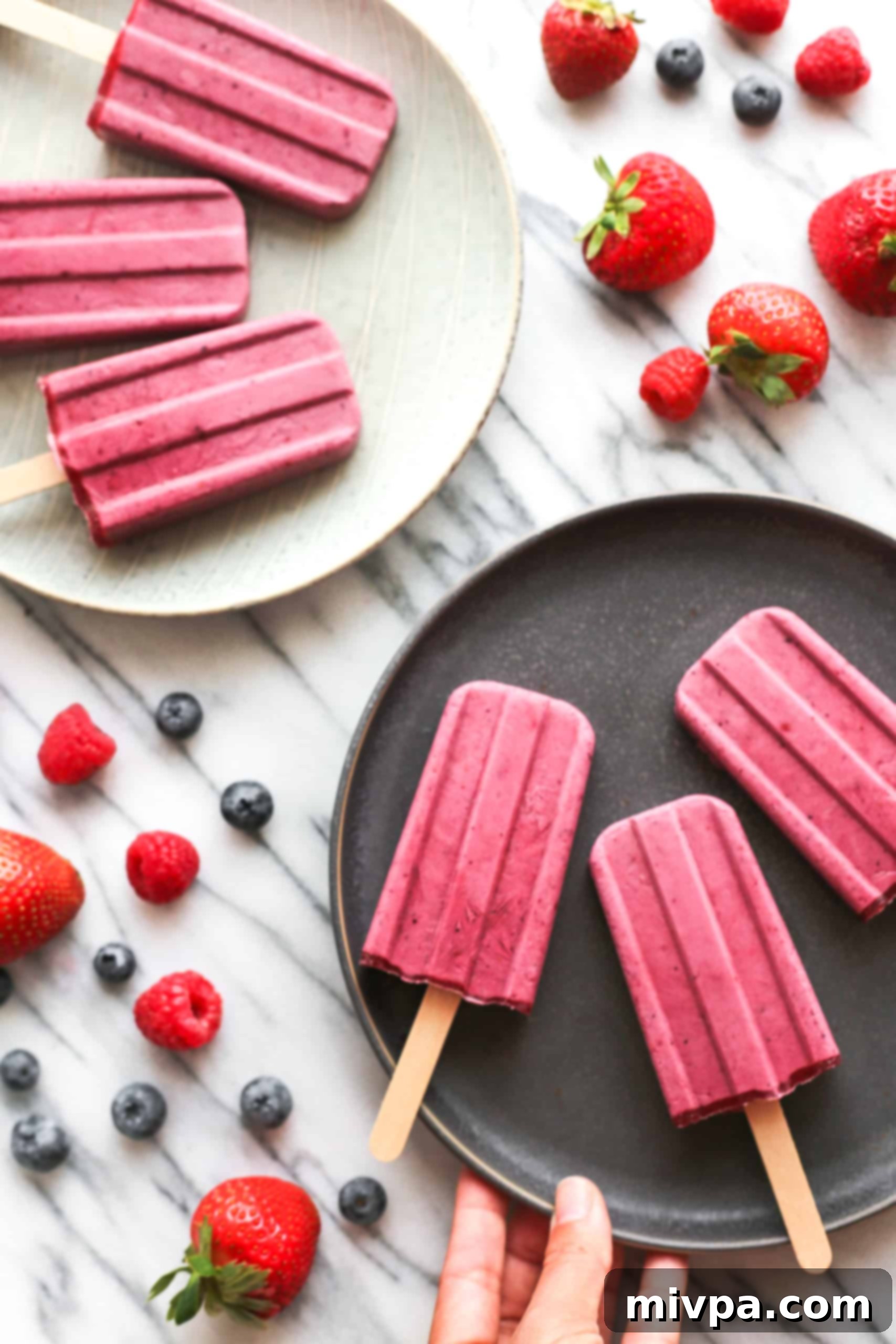 Easy Mixed Berry Yogurt Popsicles (Gluten-Free, Vegan) Holding a plate with berry yogurt popsicles.