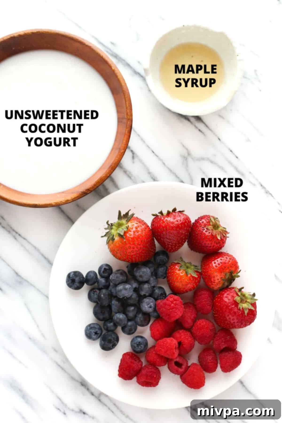 Ingredients for mixed berry yogurt popsicles laid out on a marble board, including fresh berries, coconut yogurt, and maple syrup.