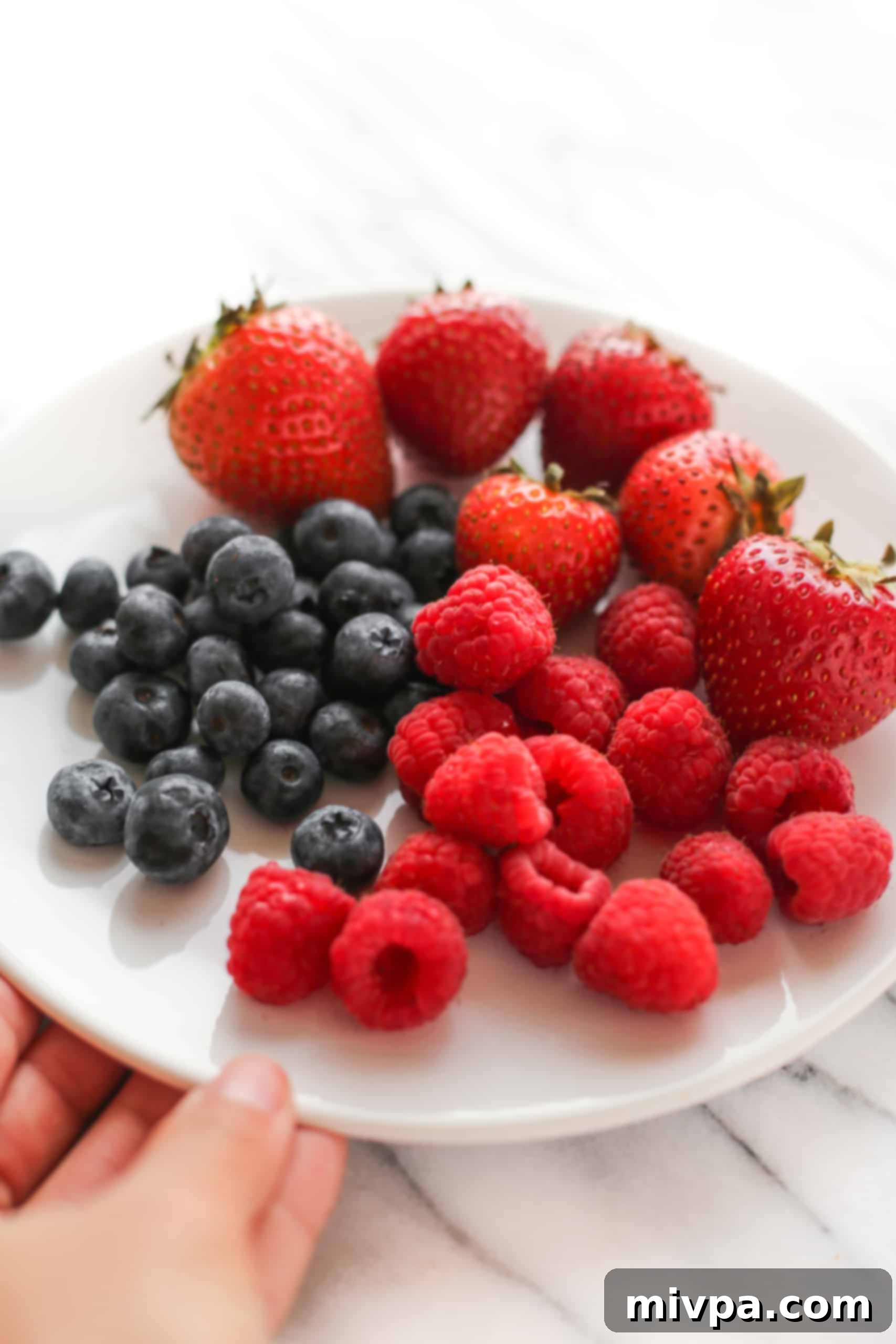 Easy Mixed Berry Yogurt Popsicles (Gluten-Free, Vegan) Hand holding a large plate with strawberries, blueberries and raspberries.