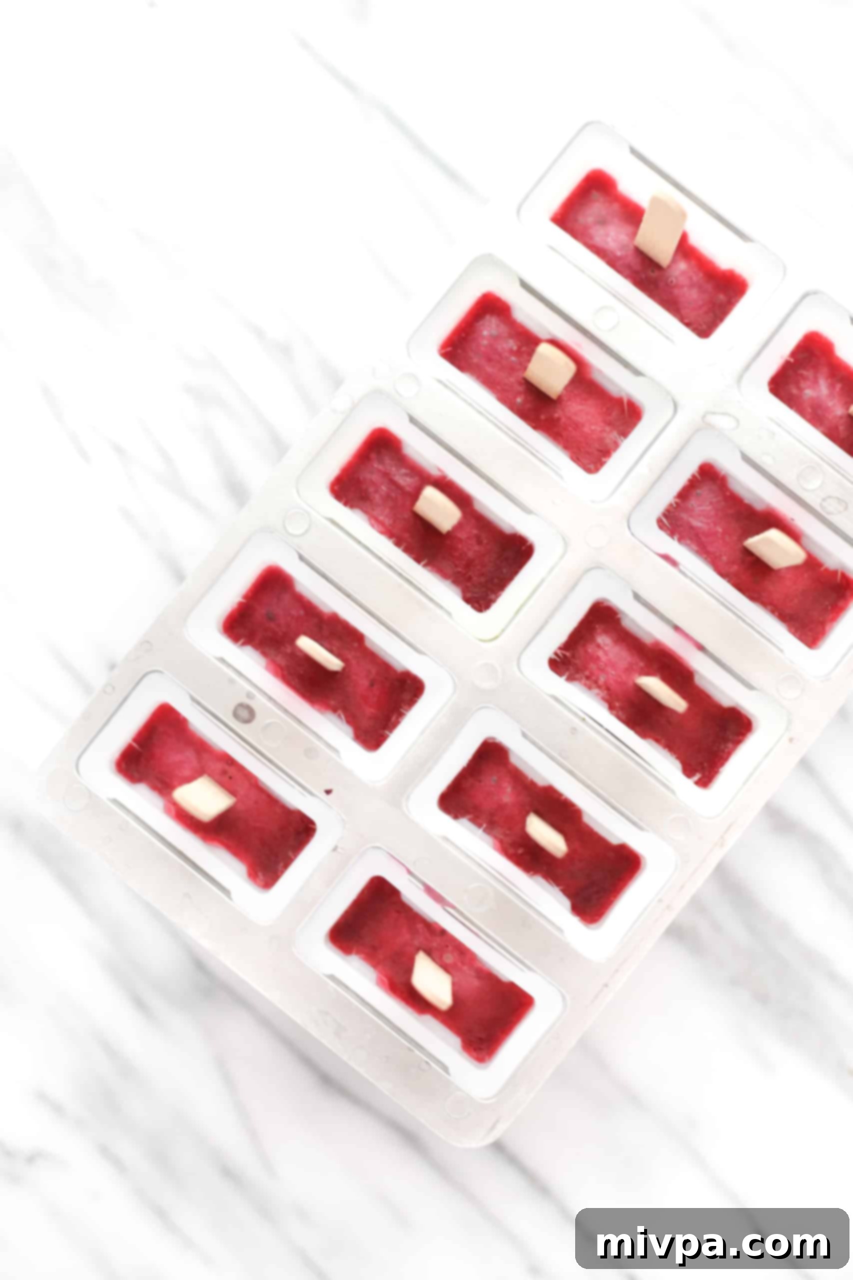 Homemade fruit popsicles partially frozen in a popsicle mold, showing the sticks inserted.