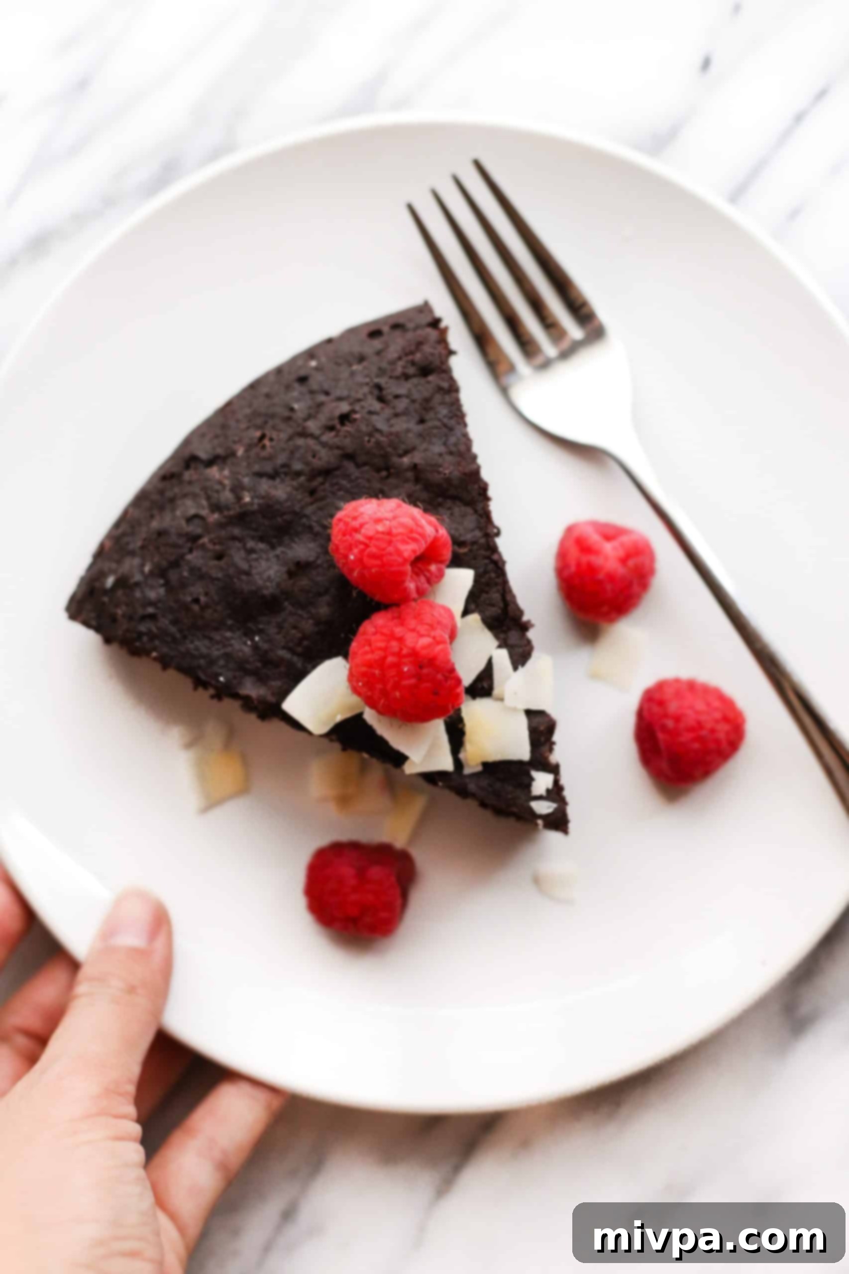Flourless Chocolate Cake (Gluten-Free, Dairy-Free) Hand holding a plate with a slice of gluten-free chocolate cake.