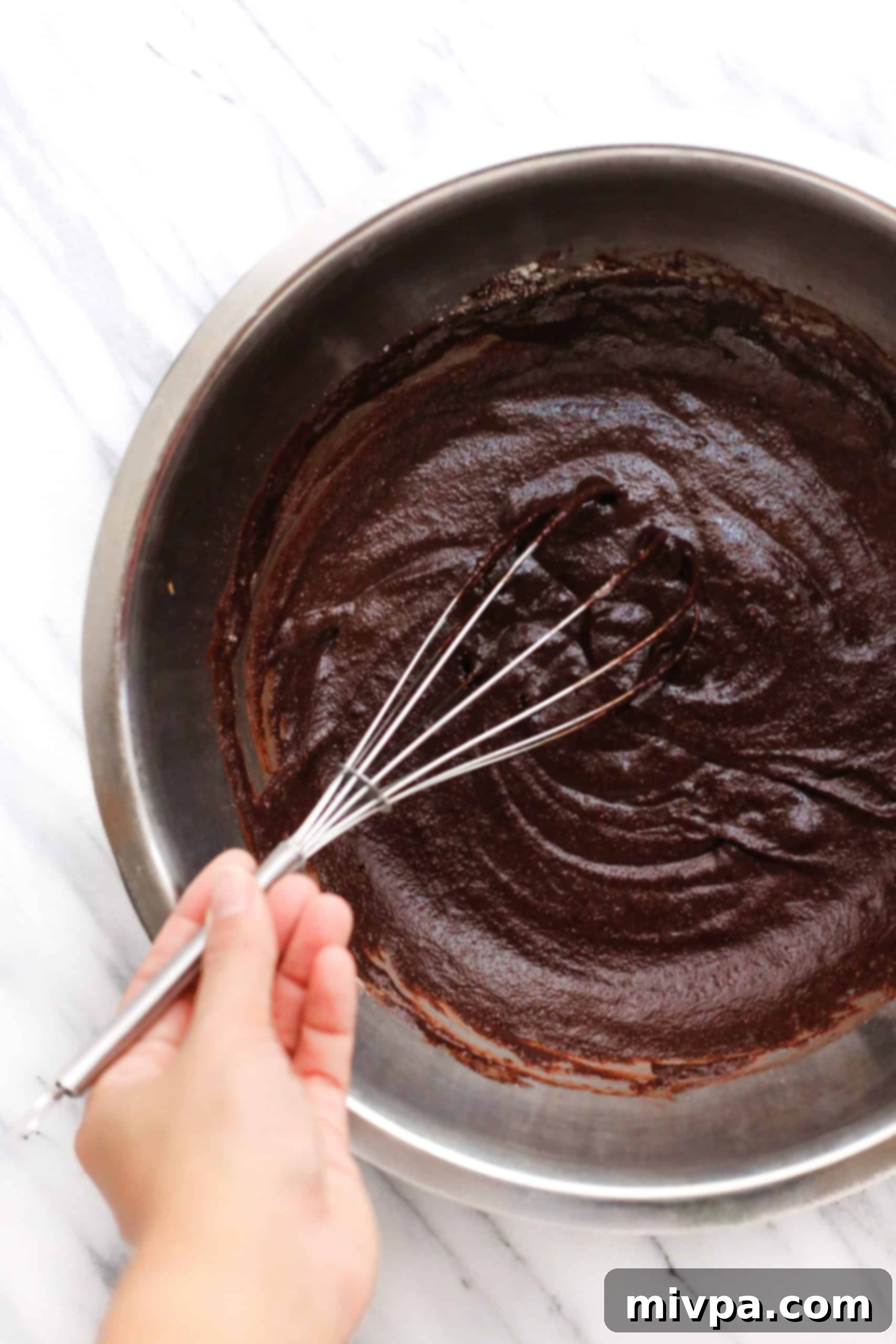 Coconut Flour Chocolate Cake (Gluten-Free, Dairy-Free) Whisking the flourless chocolate cake batter in a large metal bowl.
