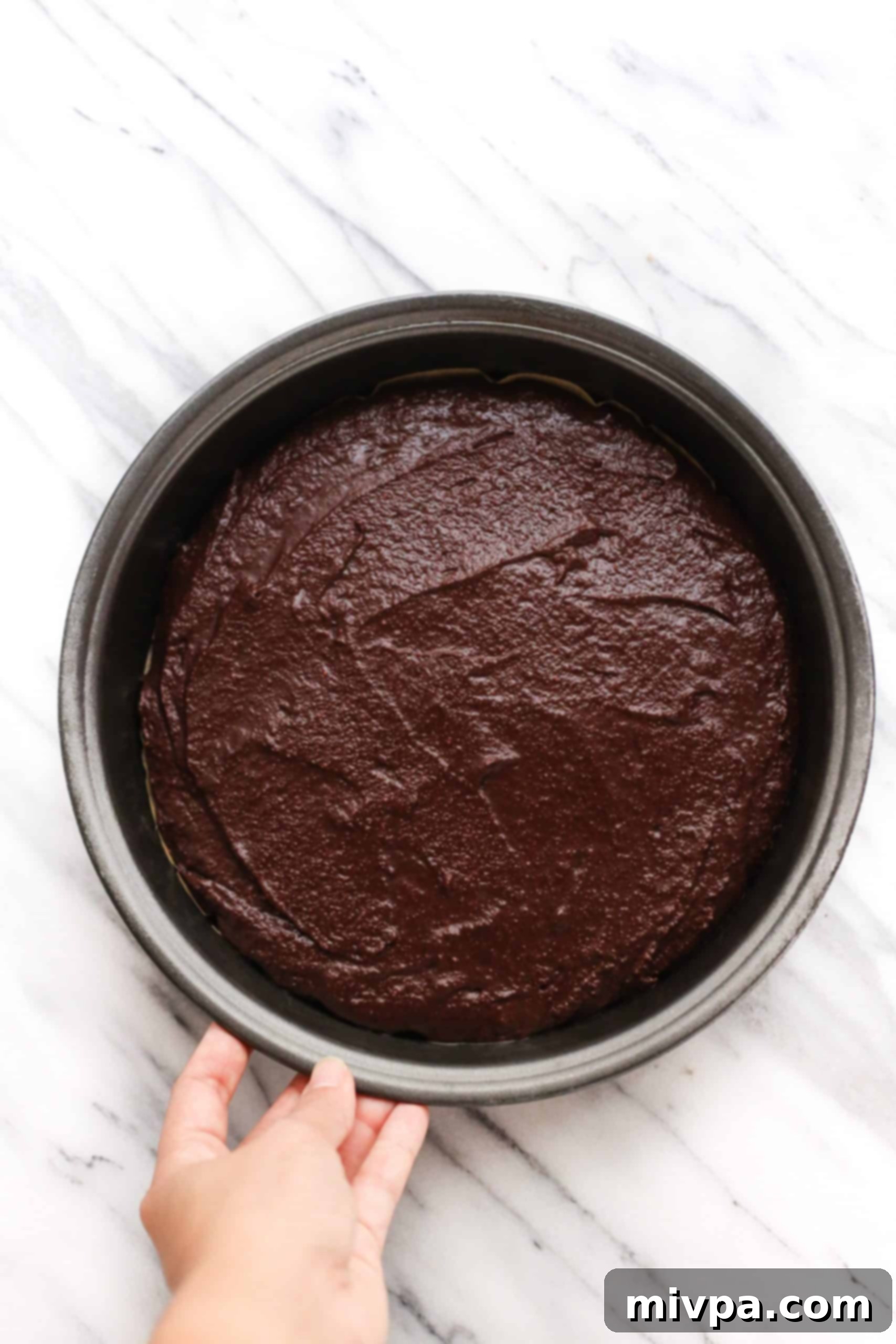 Coconut Flour Chocolate Cake (Gluten-Free, Dairy-Free) Holding a round cake pan filled with cake batter.