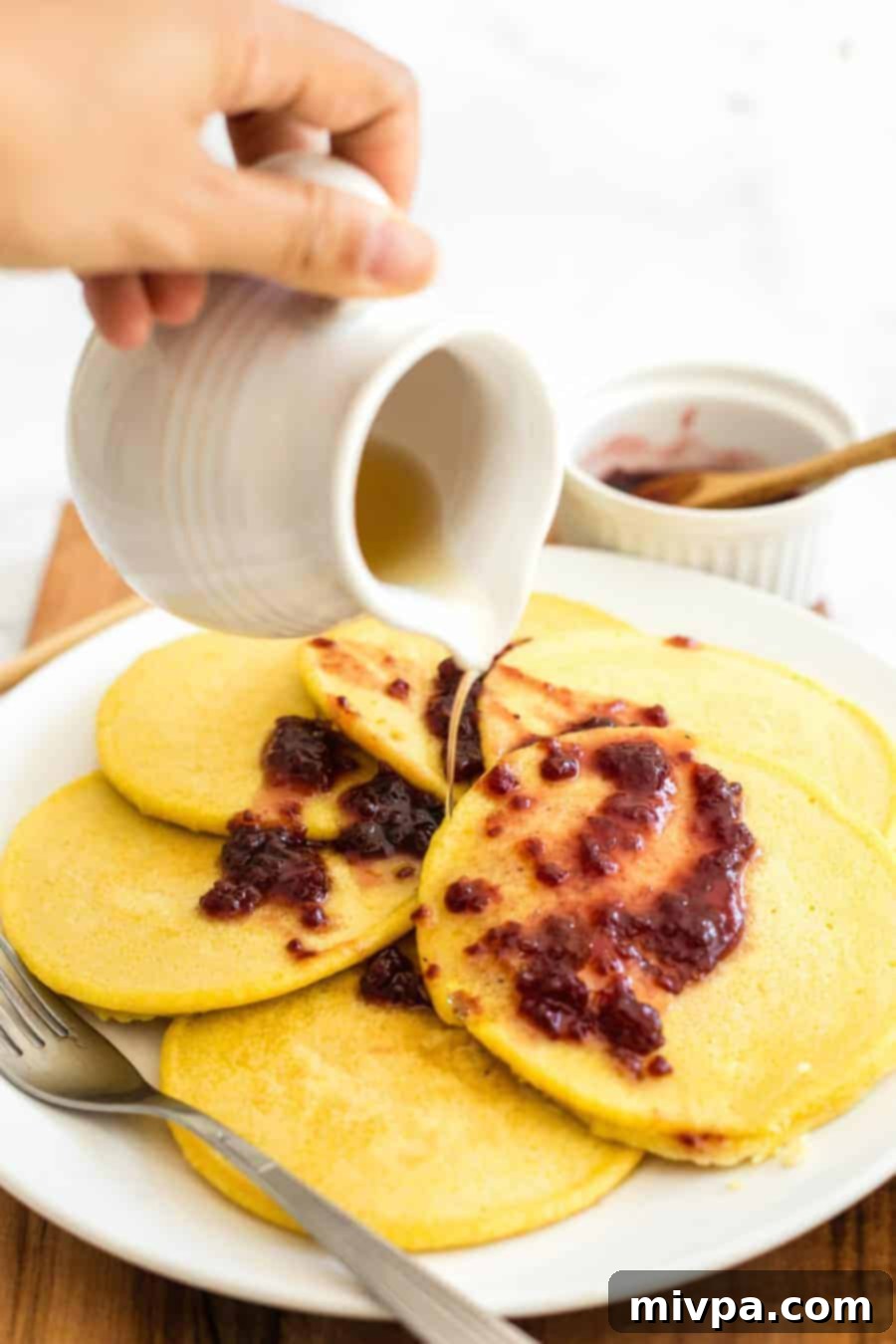 Pouring maple syrup over corn flour pancakes, highlighting their golden color and inviting texture.