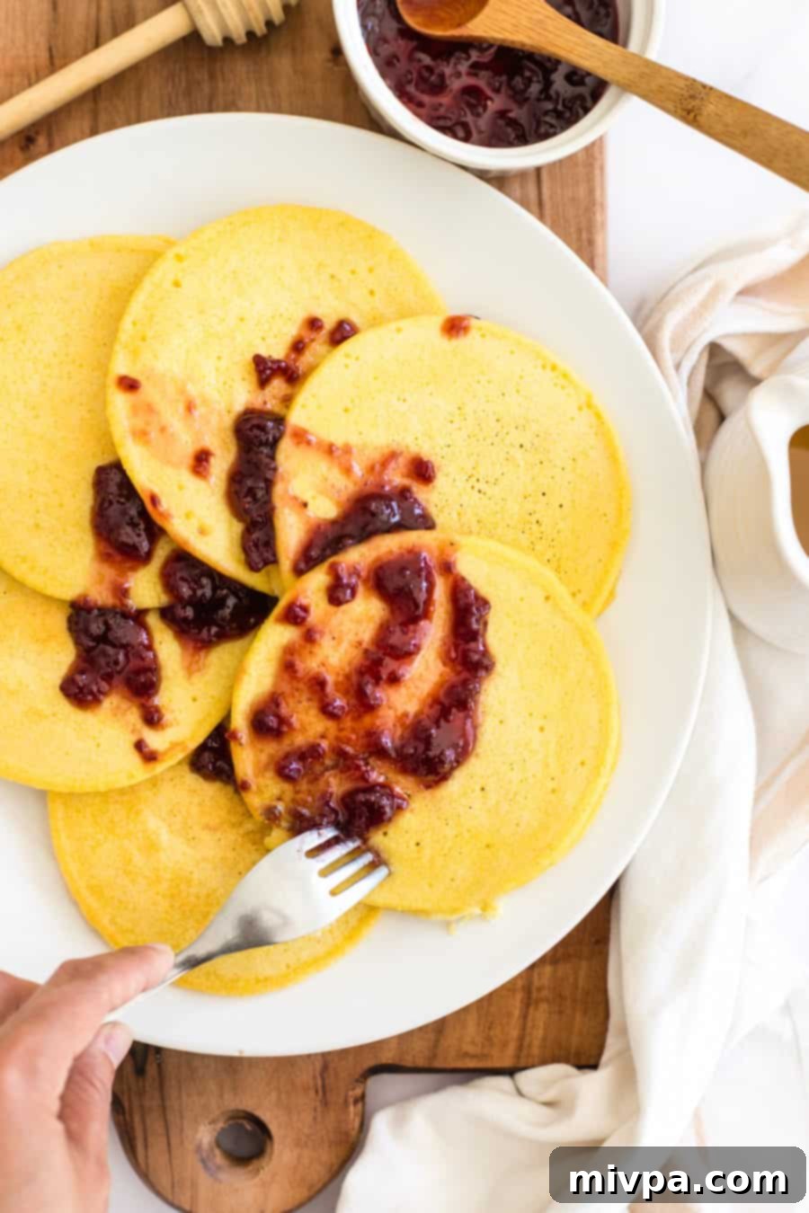 A fork poking into a stack of golden corn flour pancakes on a white plate, ready to be enjoyed.