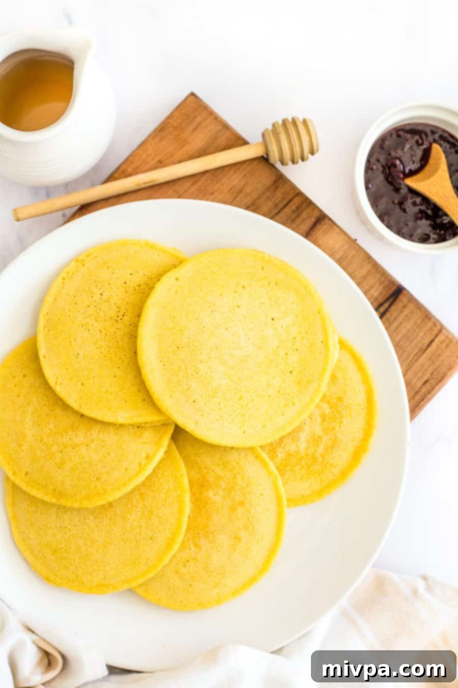 A stack of perfectly golden yellow corn flour pancakes on a plate, ready for toppings.