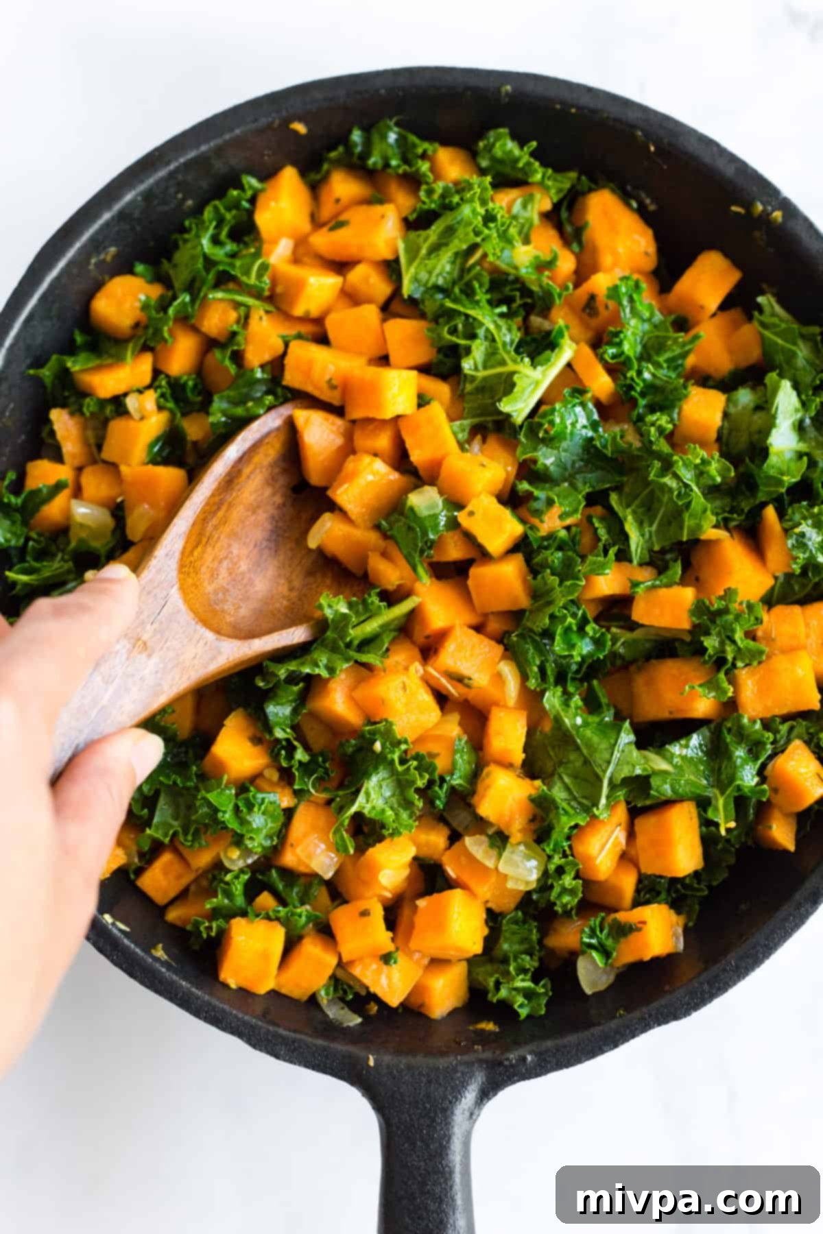 Wilted kale leaves mixed with tender sweet potatoes and onions in a skillet.