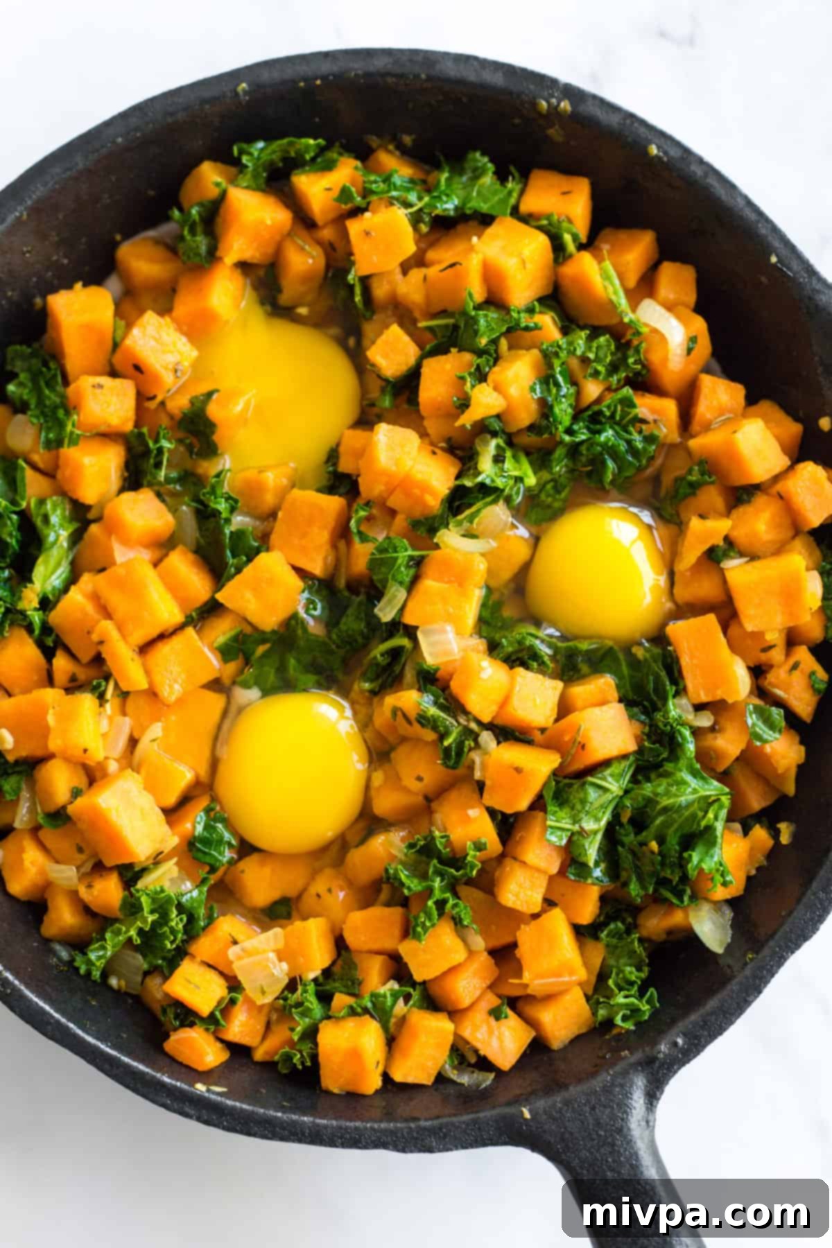 Three eggs nestled in sweet potato and kale hash, cooking in a skillet.