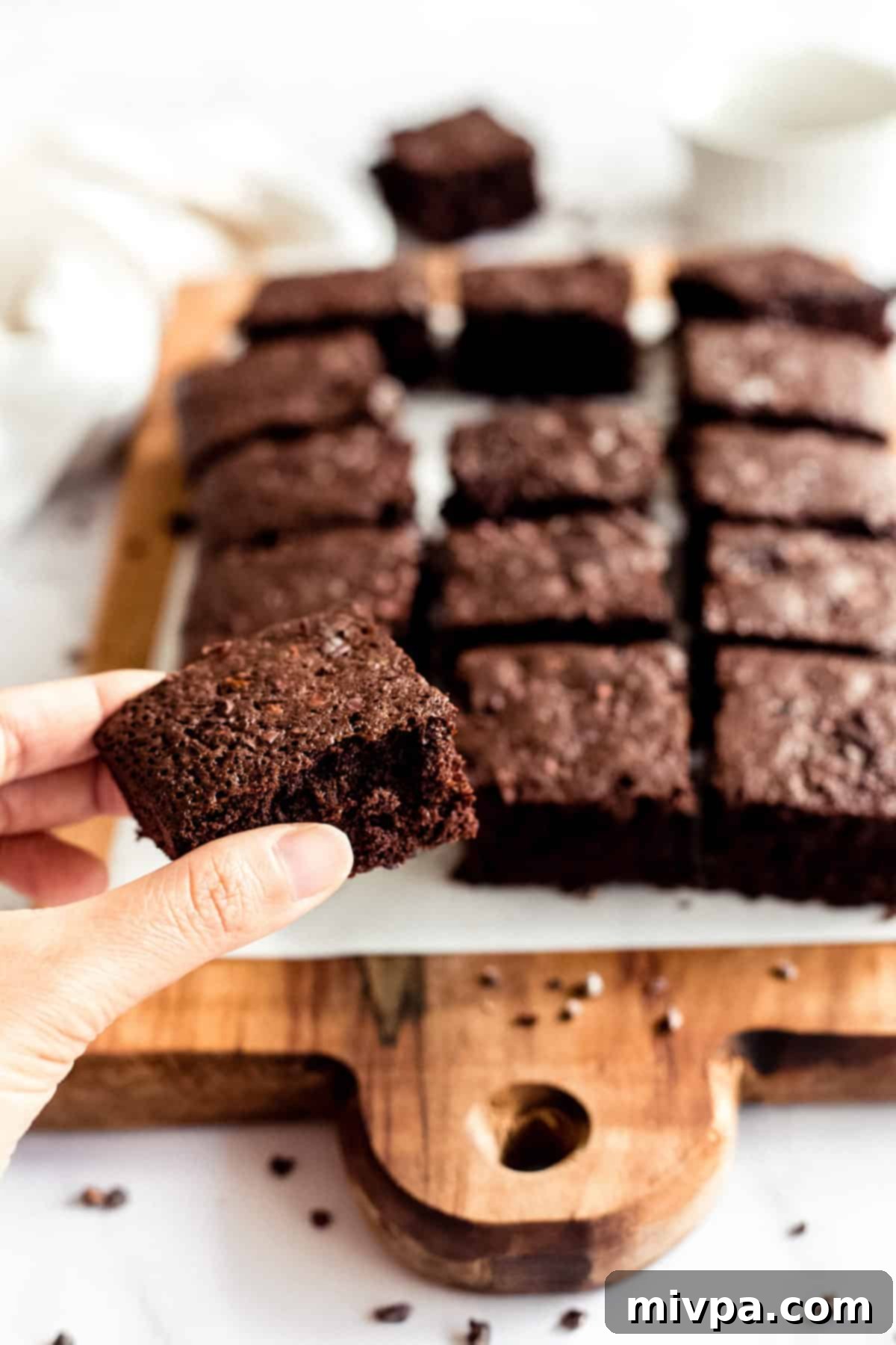 A hand holding up a perfectly fudgy gluten-free dairy-free brownie square, showcasing its rich texture and shiny top.