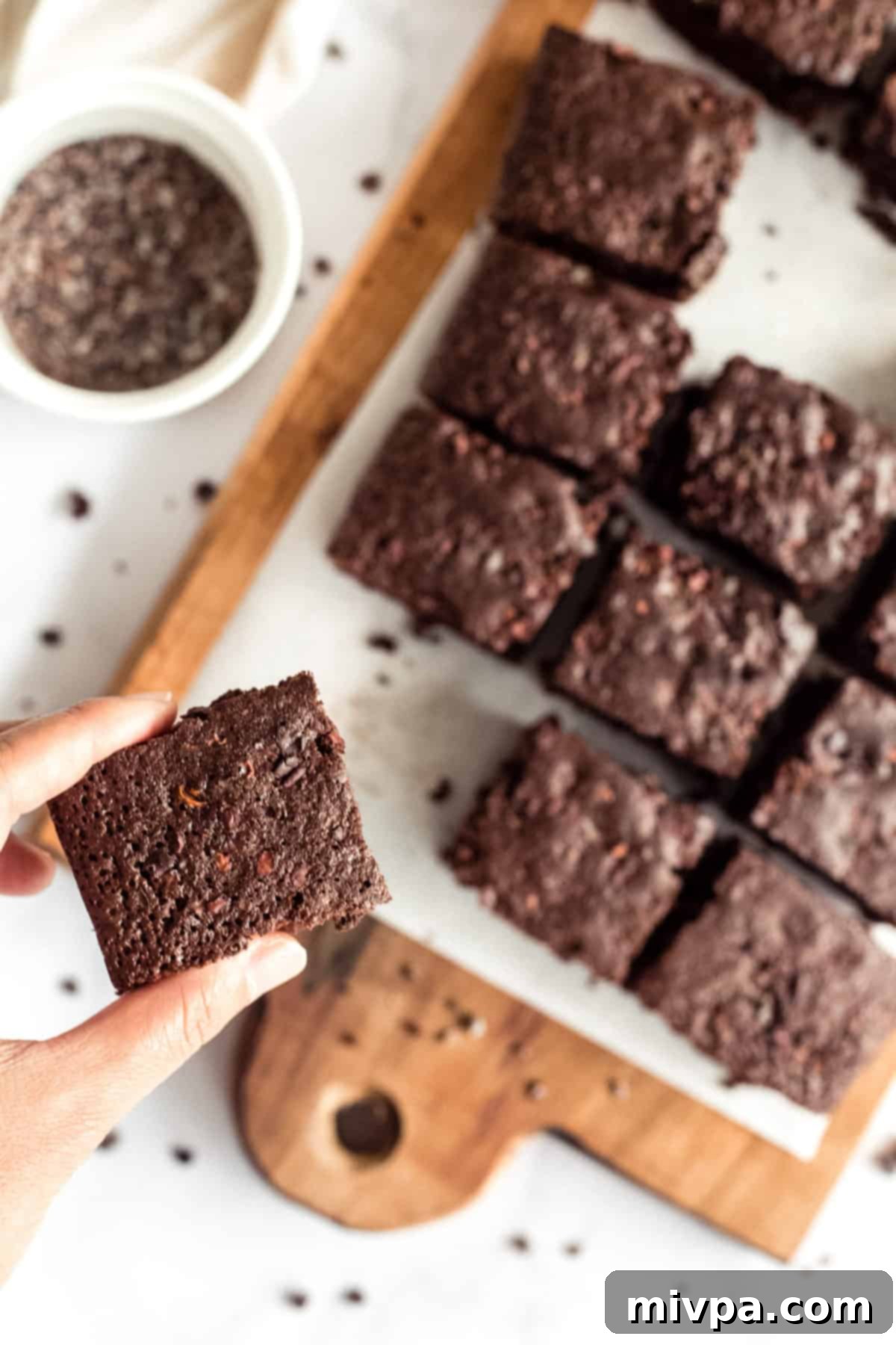 A hand holding up a freshly baked gluten-free dairy-free brownie, showcasing its perfect fudgy center and shiny crinkly top.