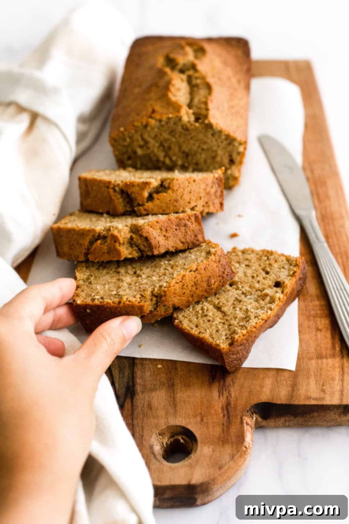 Hand reaching for a slice of gluten-free banana bread.