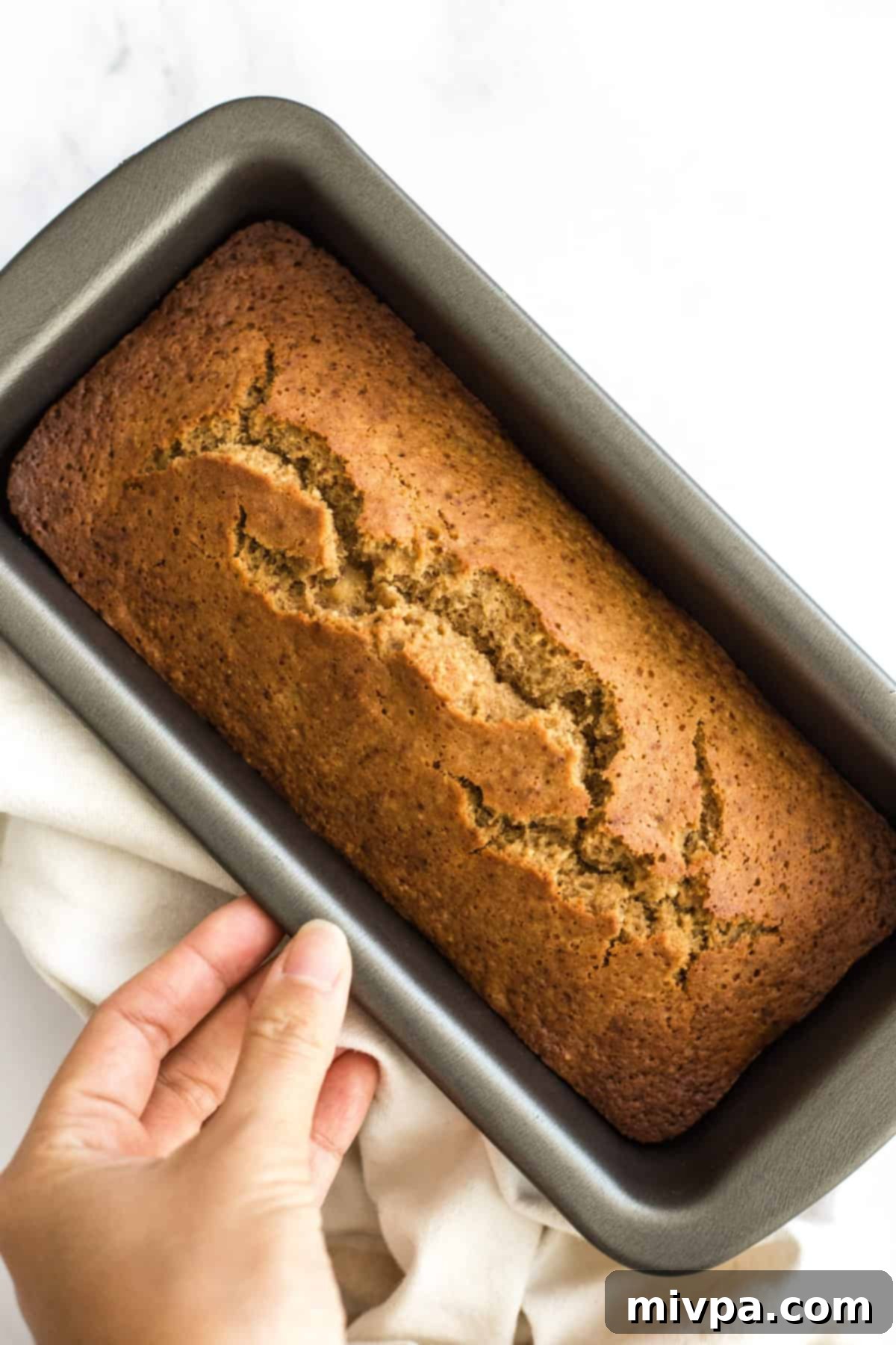 Hand holding a loaf pan with banana bread.