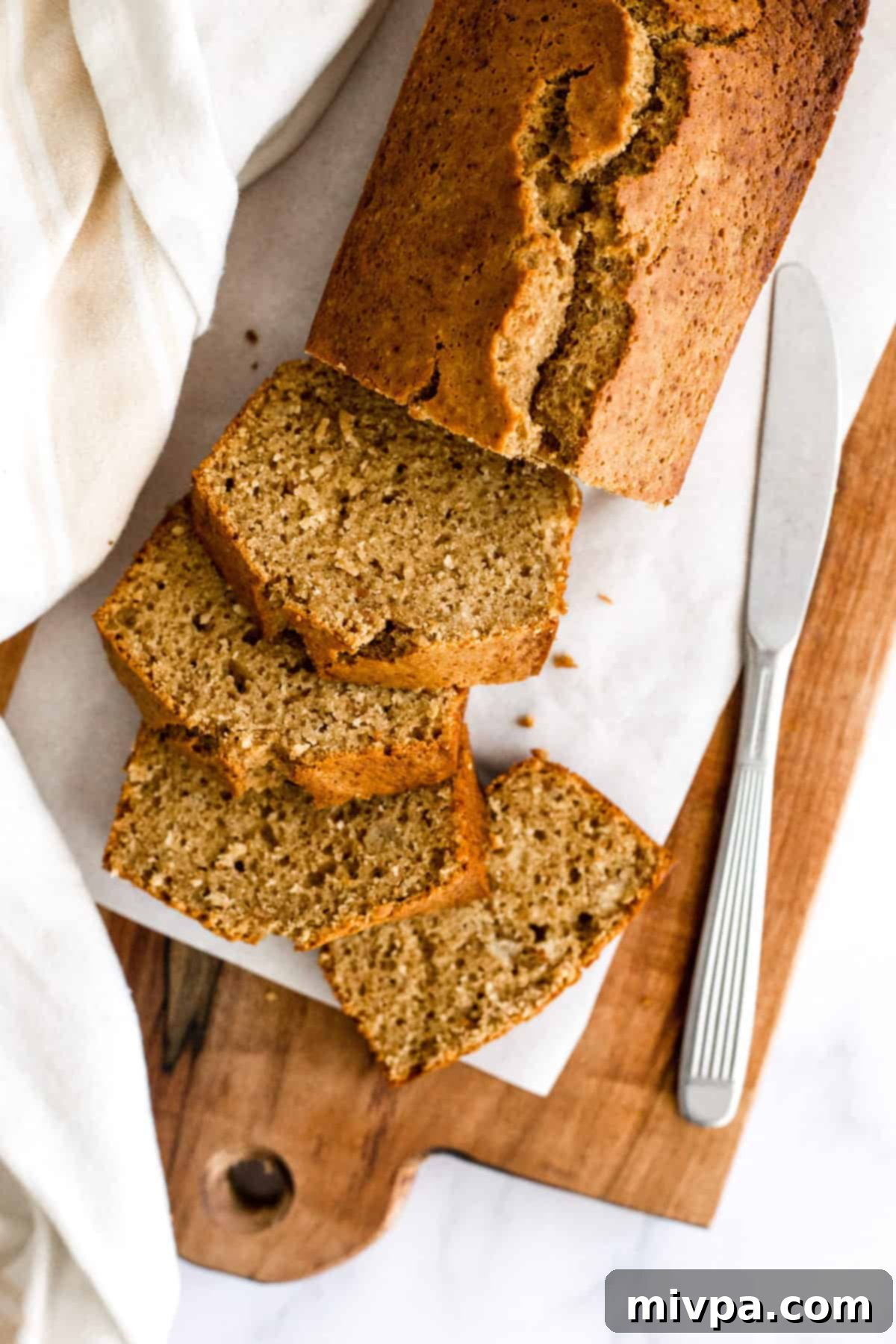 A sliced loaf of banana bread on a parchment-lined wooden board.