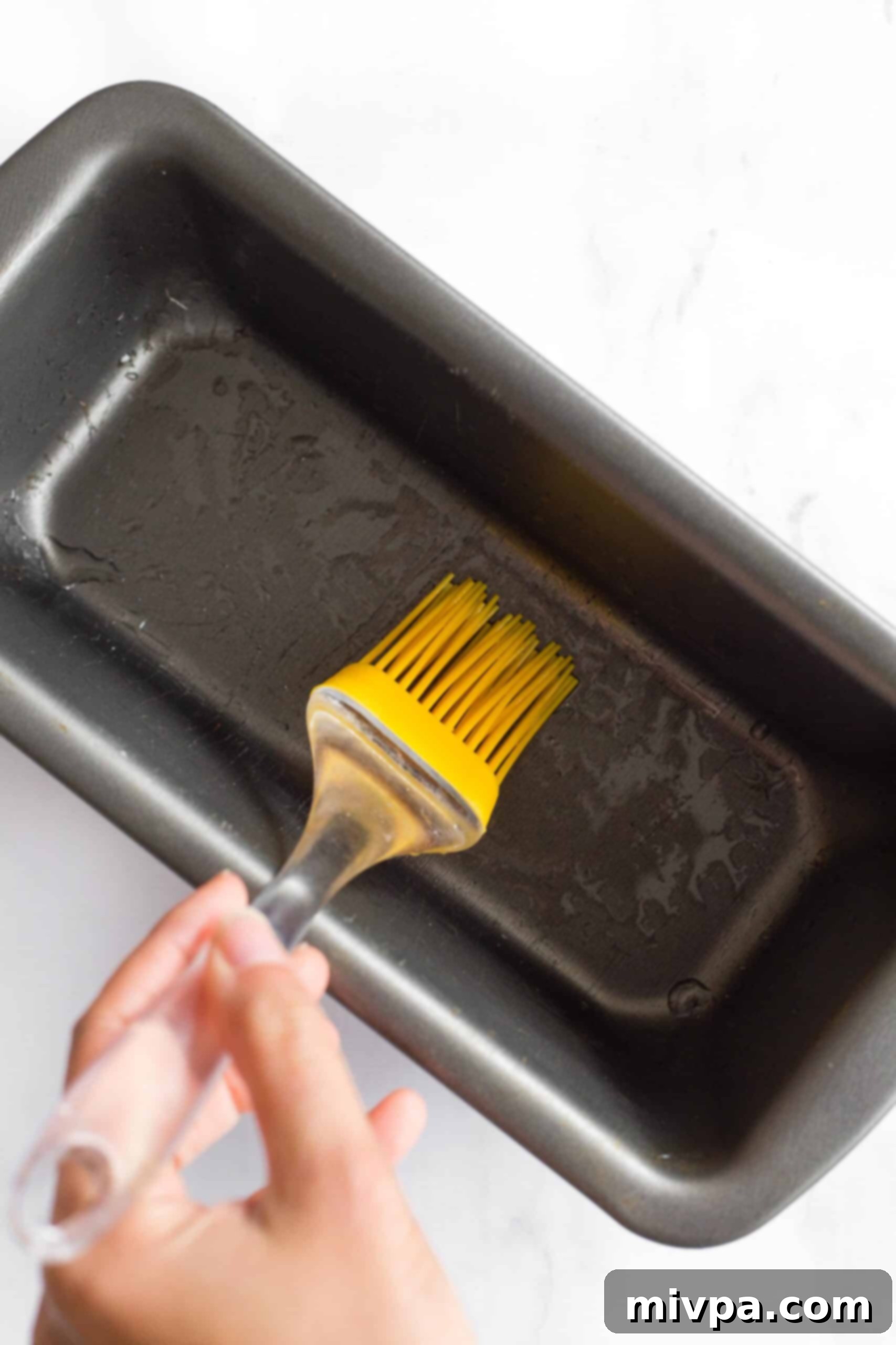 Using a silicon brush to grease a metal loaf pan.