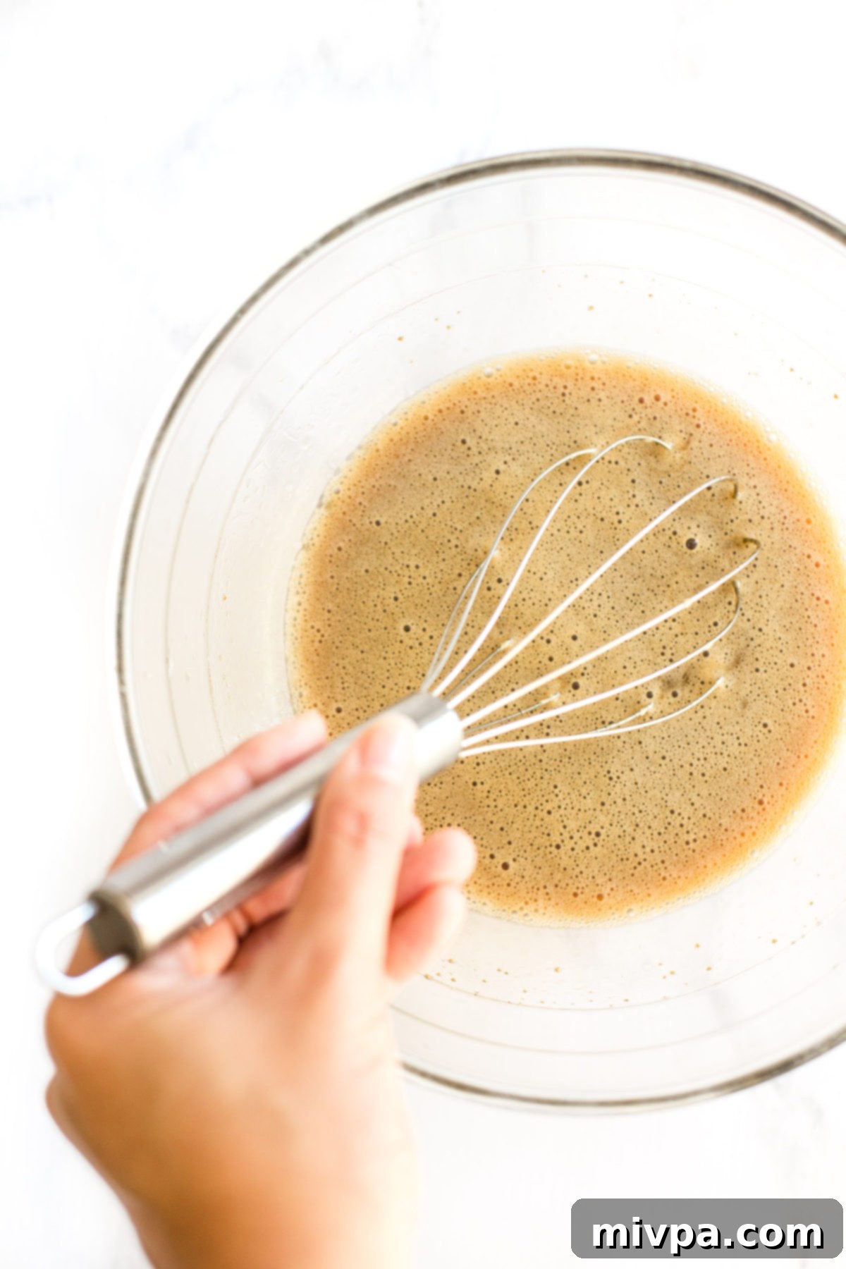 Hand whisking wet ingredients in a glass bowl.