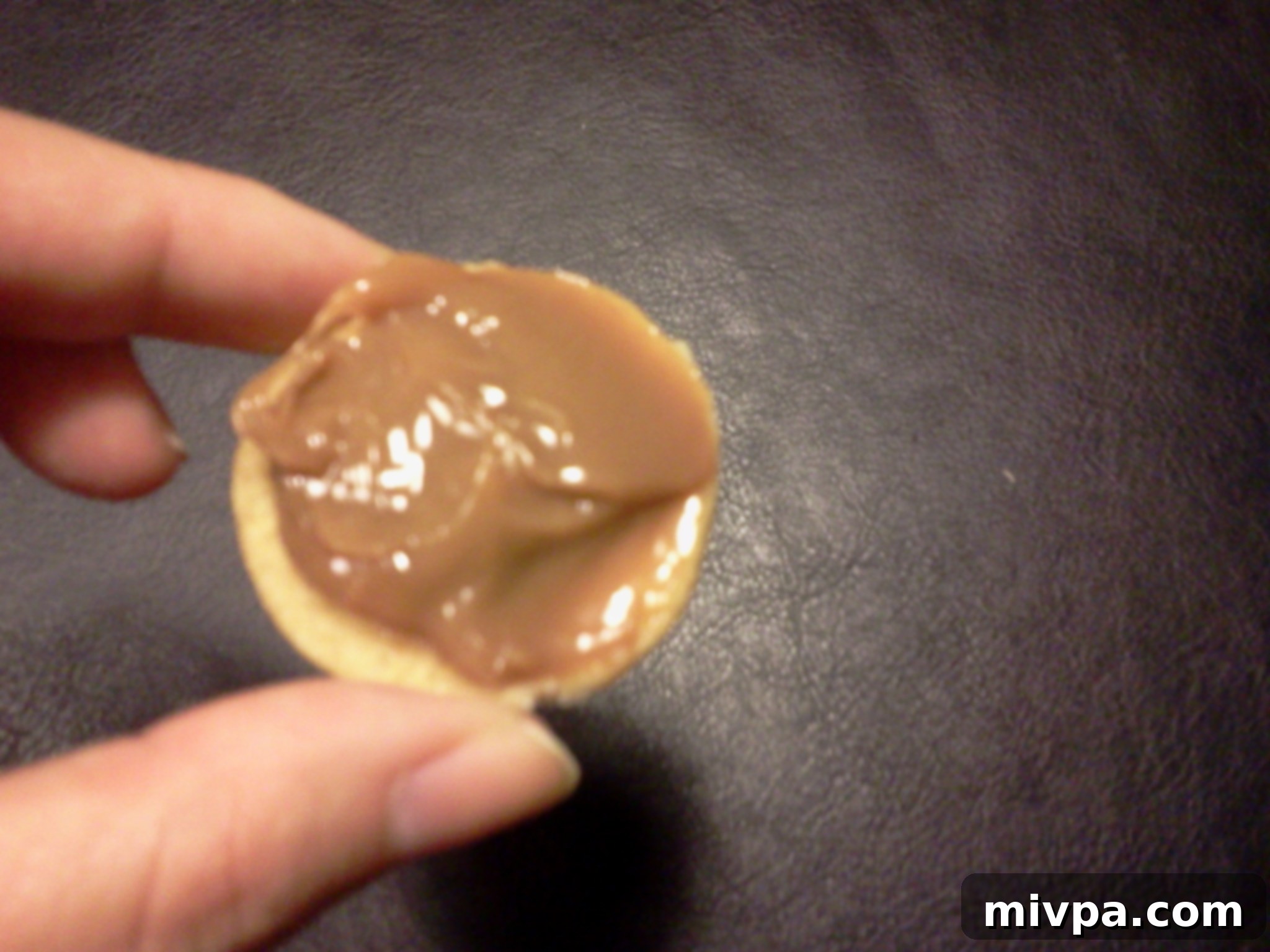 A spoon applying a thick, generous layer of creamy dulce de leche onto the flat side of a cooled, freshly baked cookie.
