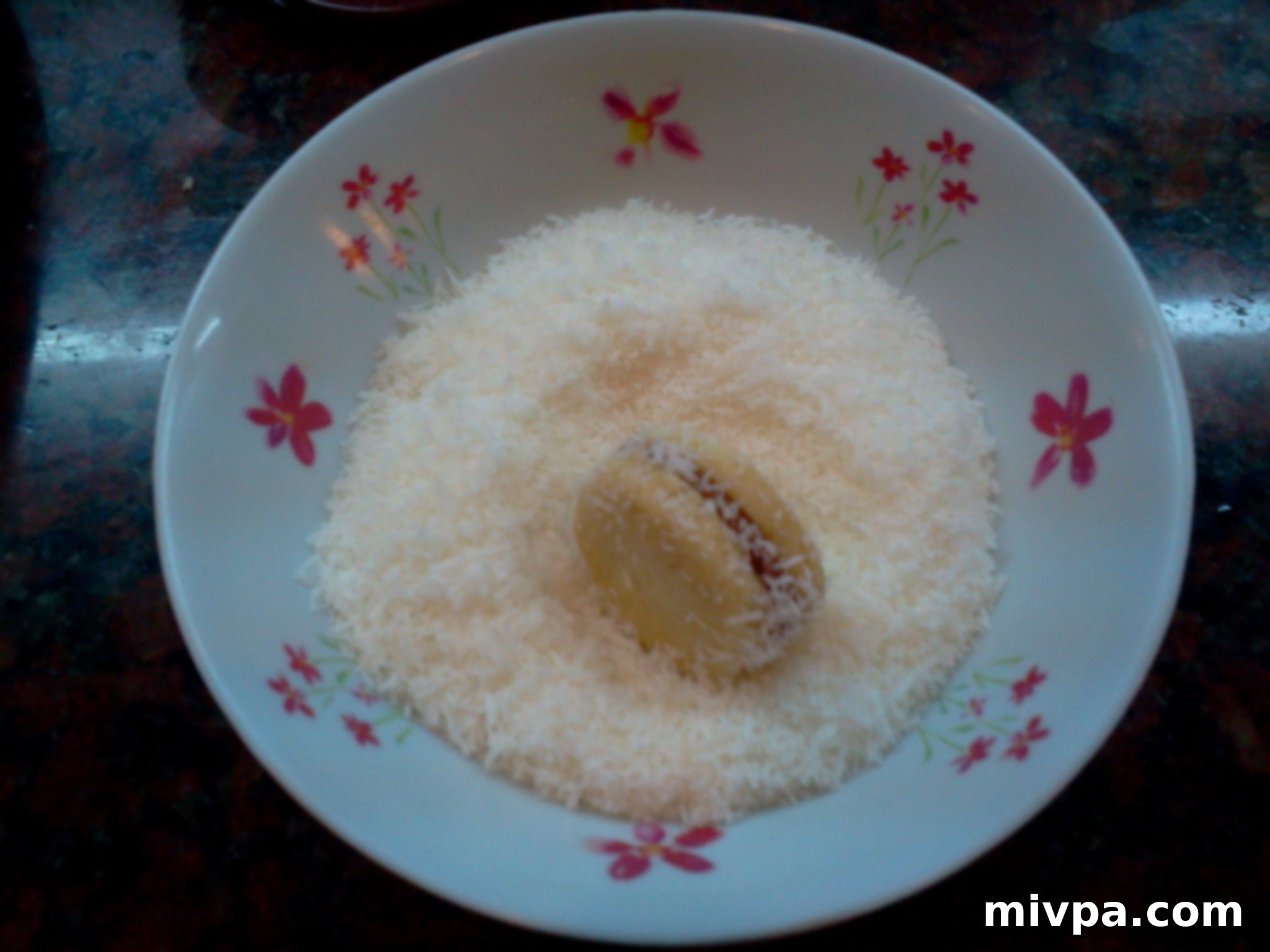 Two cookies sandwiched together with dulce de leche, being carefully rolled in shredded coconut to coat the exposed filling around the edges.
