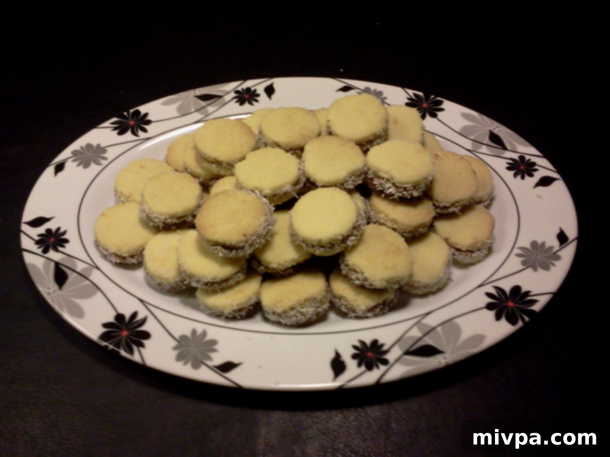 A beautiful plate showcasing a collection of freshly made Dulce de Leche Alfajores, perfectly assembled and coated with shredded coconut, ready to be enjoyed.