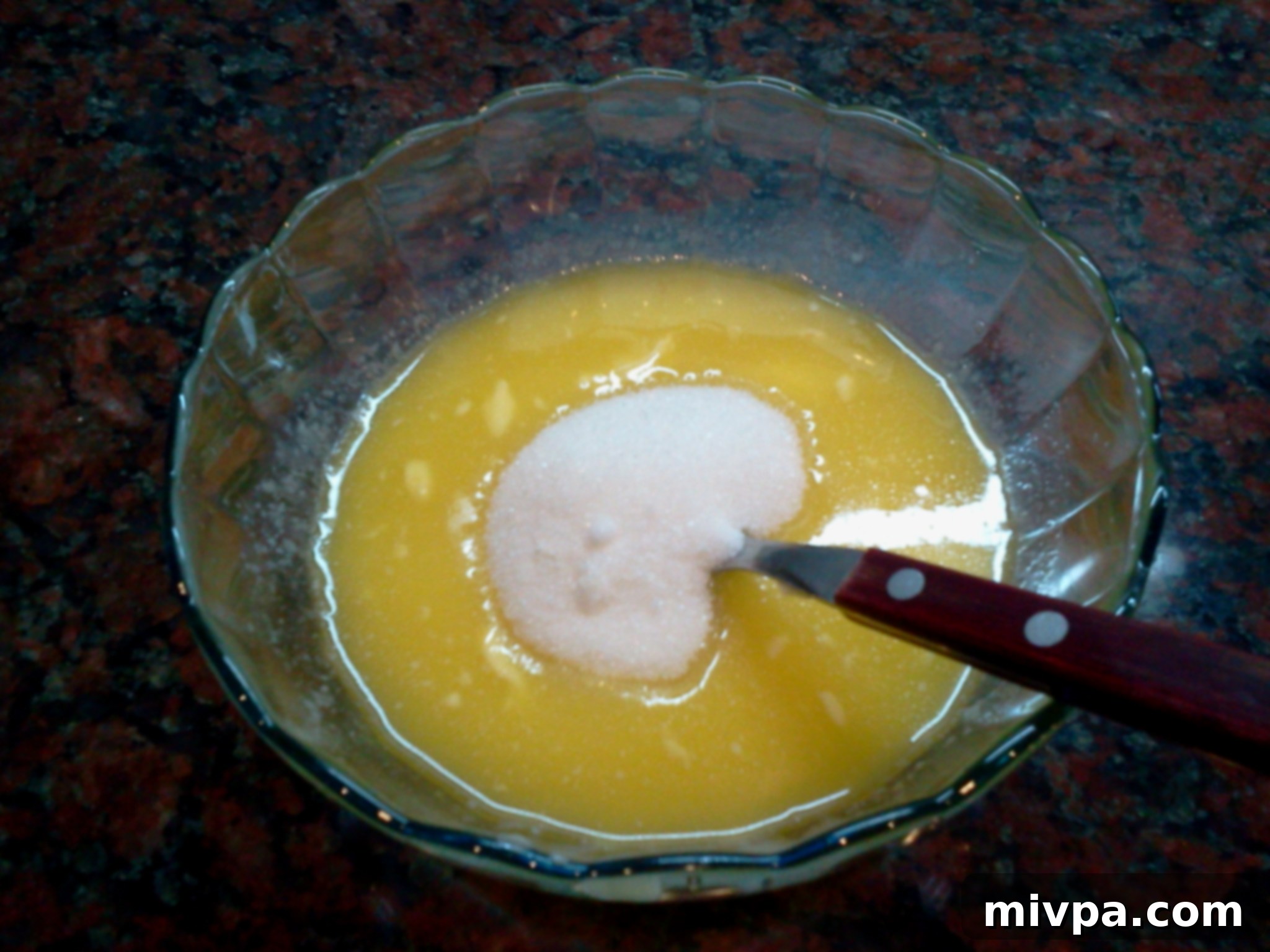 Granulated white sugar being carefully stirred into the warm melted butter until it fully dissolves, creating a sweet base for the cookies.