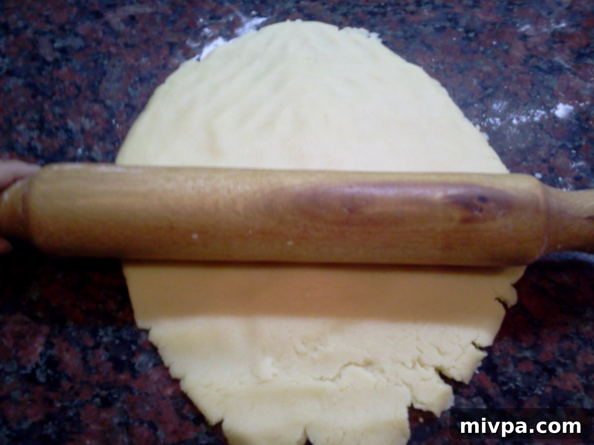 Cookie dough being gently flattened with a rolling pin to an even thickness, crucial for perfectly shaped and baked alfajores.