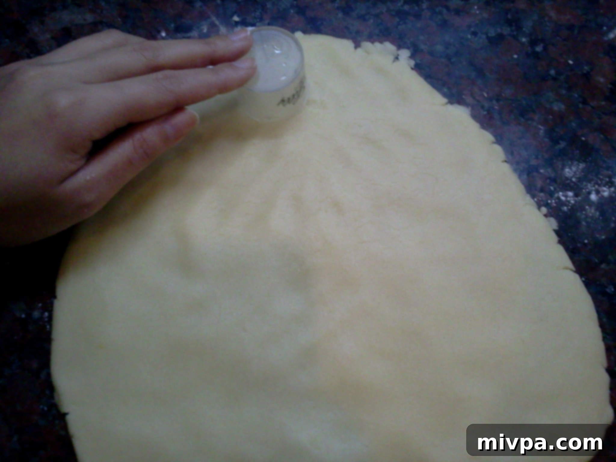 A round cookie cutter being used to precisely cut out individual cookie dough pieces, forming the classic alfajor shape.