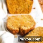 Half-sliced loaf of carrot bread on parchment paper.
