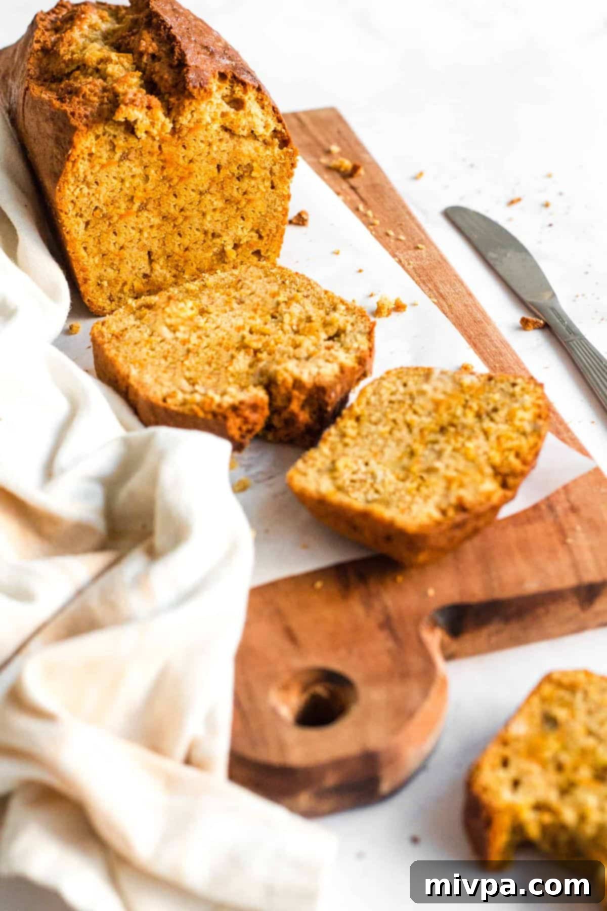 A half-sliced loaf of gluten-free carrot cake bread on parchment-lined board.