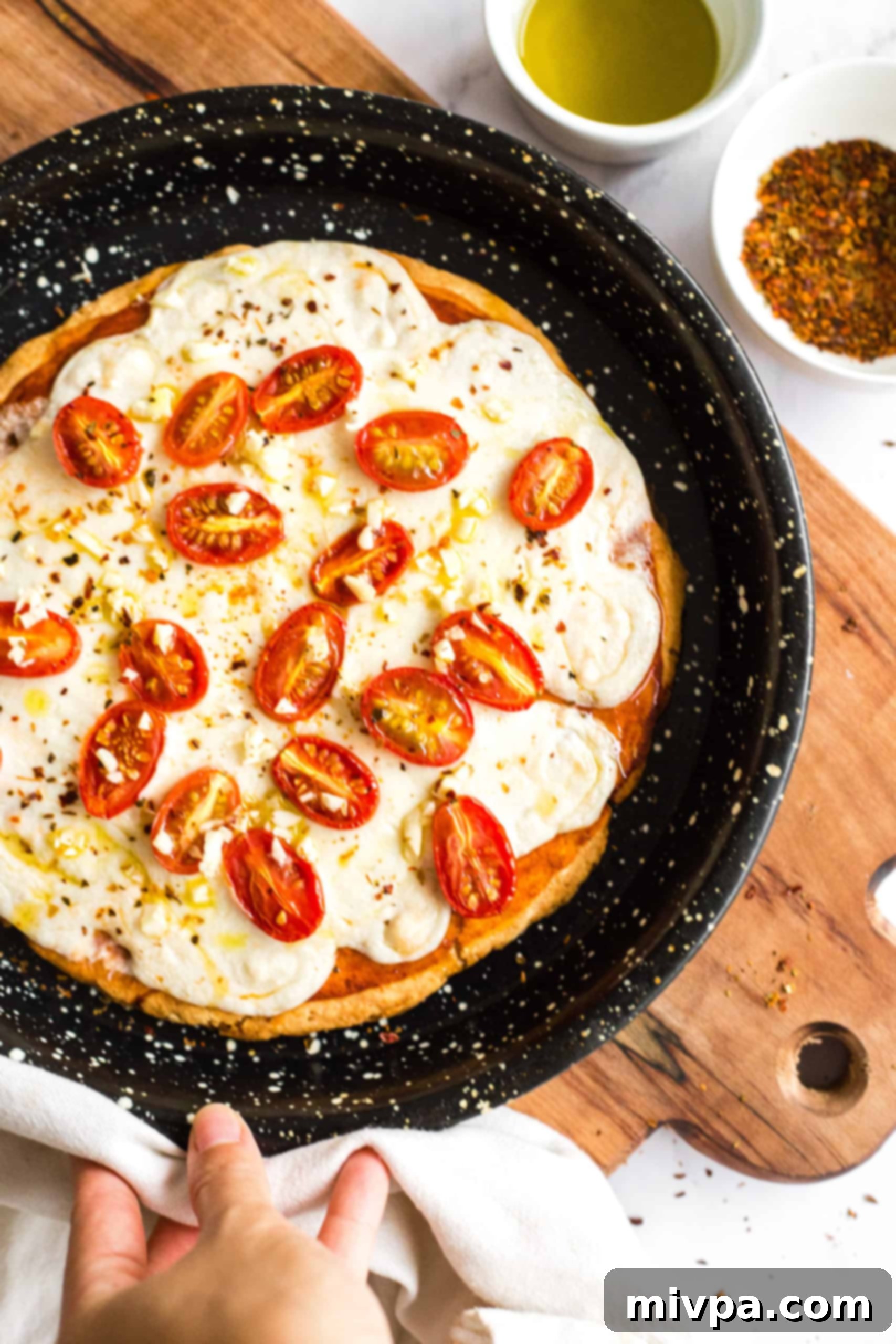 Hand holding gluten-free pizza in a pizza pan on a wooden board.