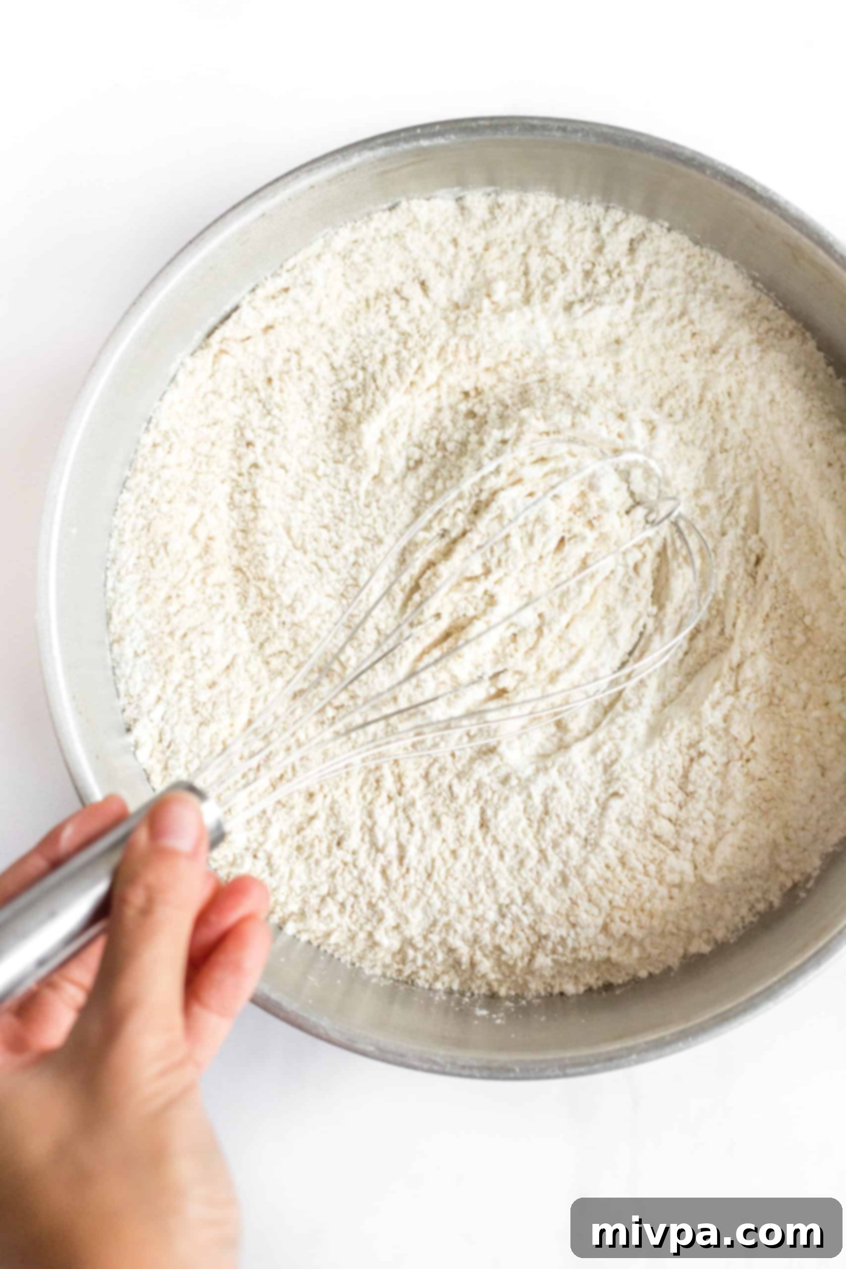 A hand whisking gluten-free all-purpose flour, brown rice flour, and salt together in a large mixing bowl.